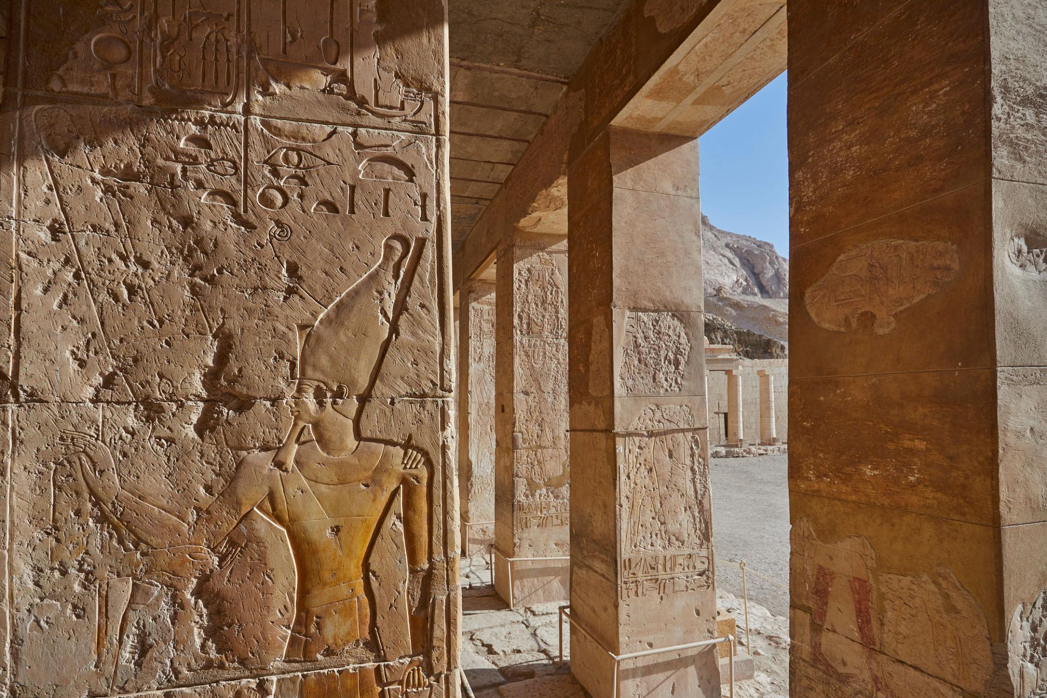 Carved relief of pharaoh with double crown beside temple portico opening to valley