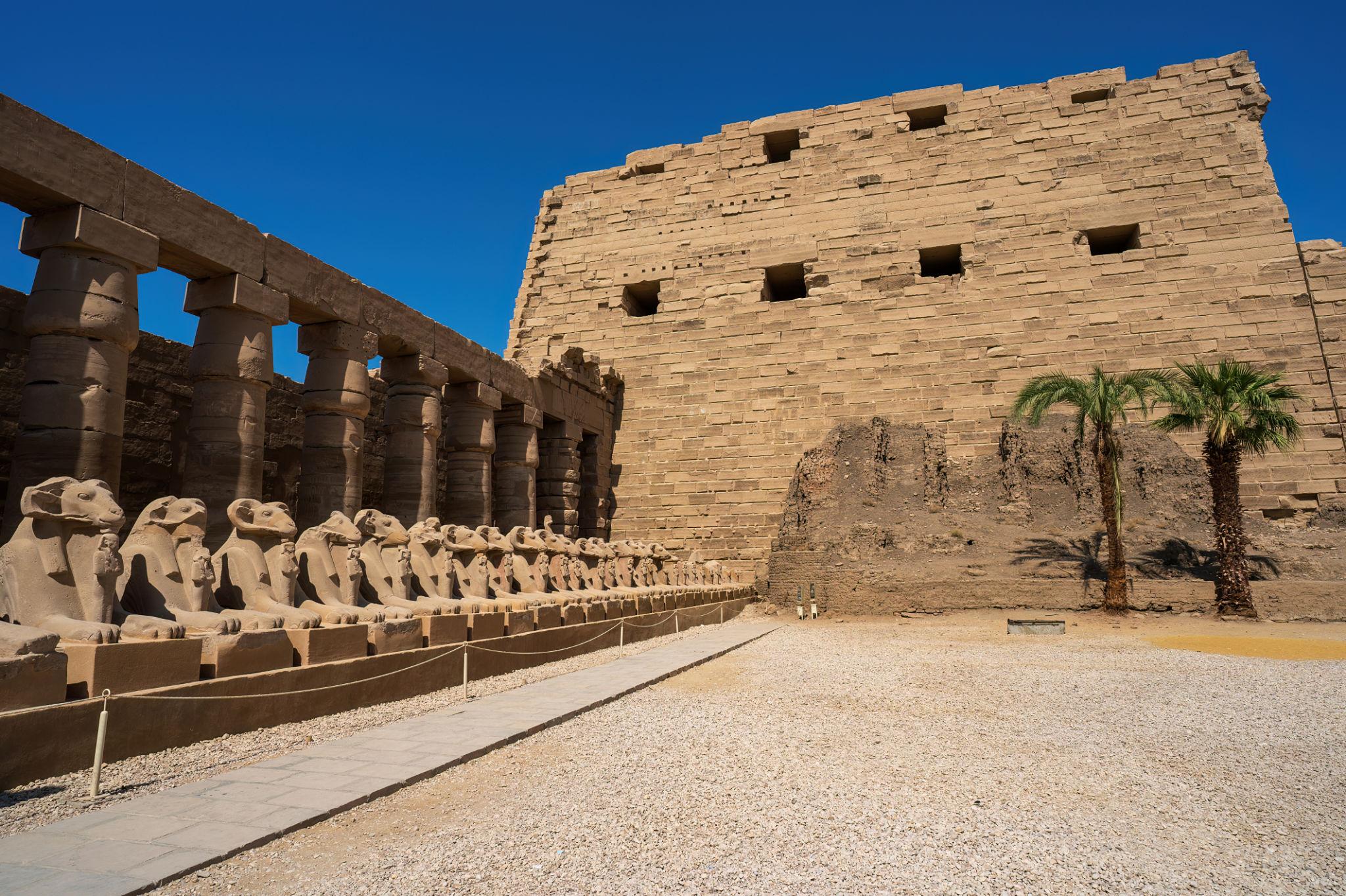 Ram-headed sphinxes beside the massive pylon wall of Karnak Temple