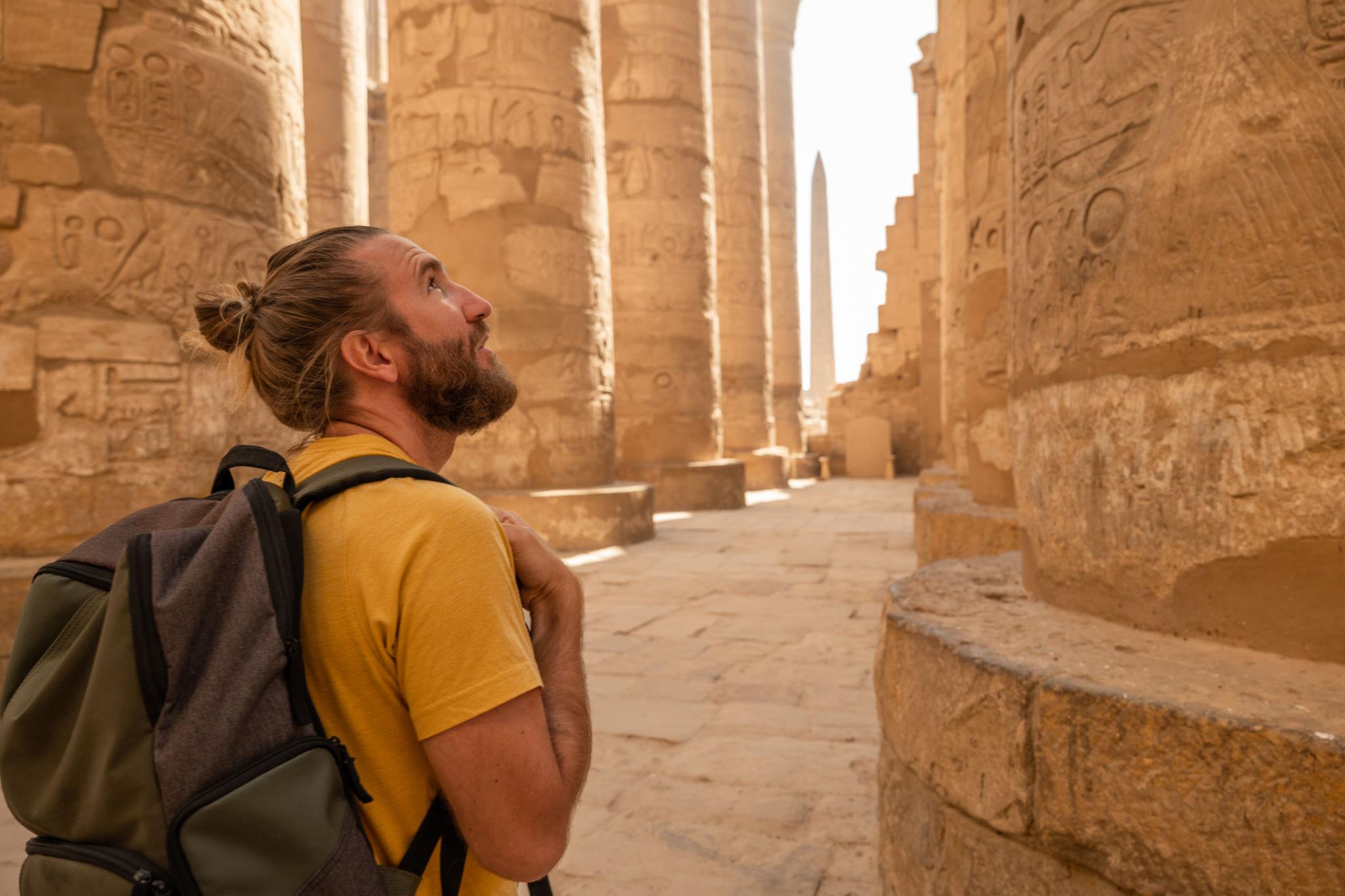 Traveler in yellow shirt gazing up at columns in Karnak's Hypostyle Hall