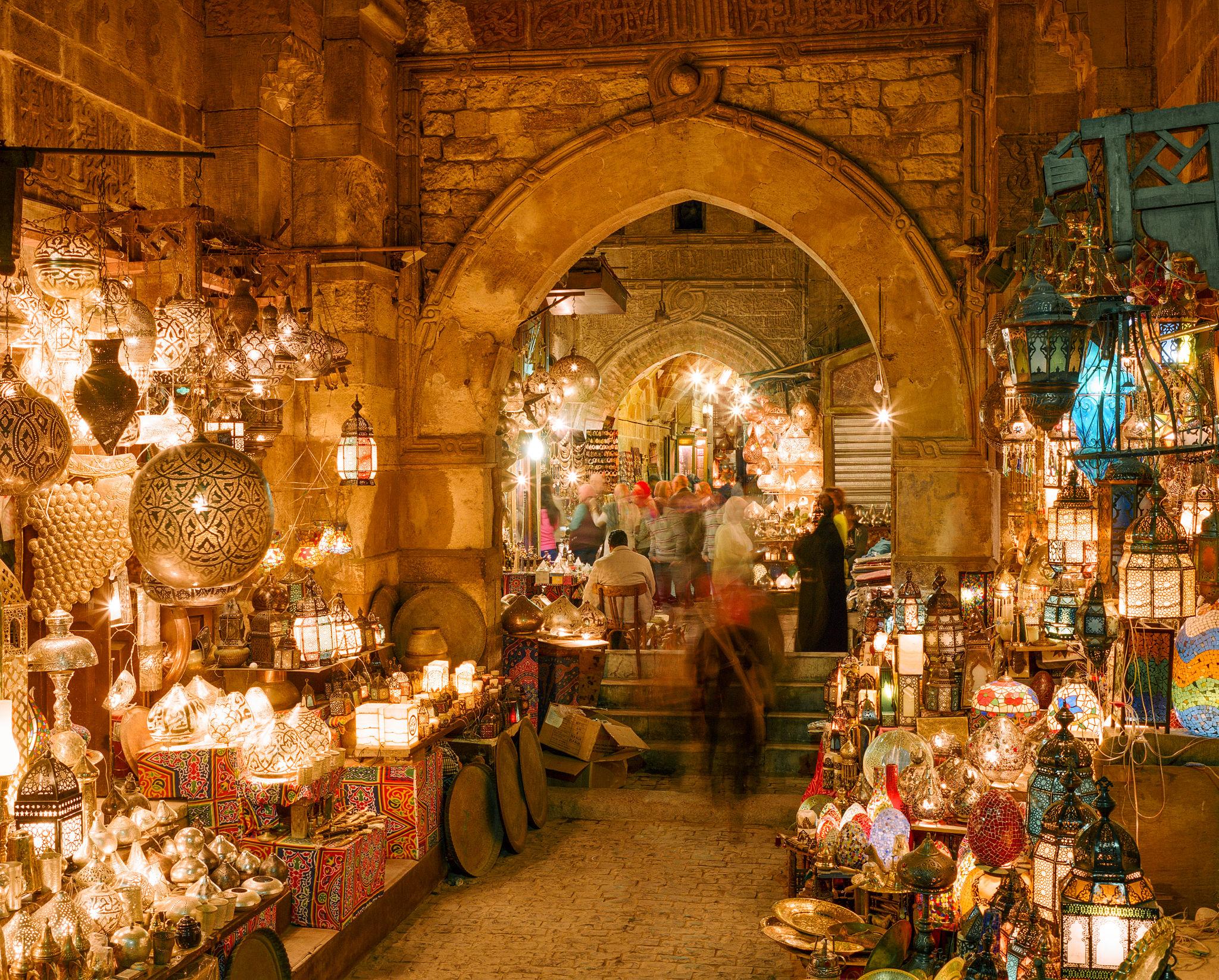 Ornate brass and mosaic lanterns illuminate a medieval stone archway at Khan el-Khalili bazaar