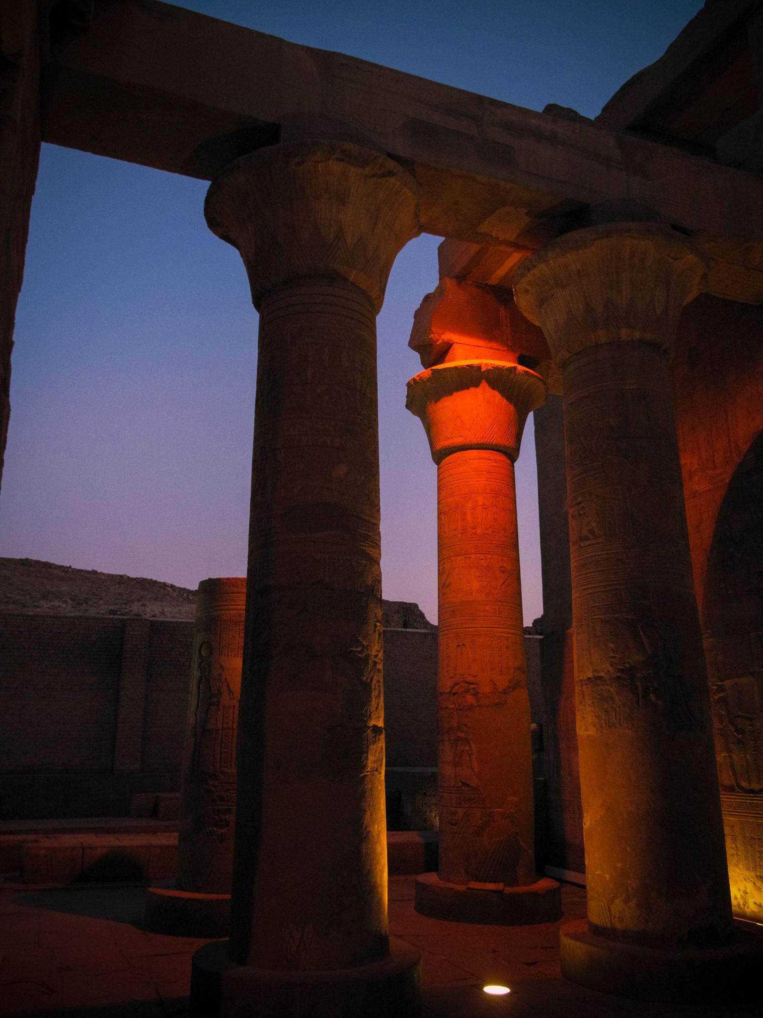 Stone columns at Kom Ombo Temple uplit against a deep blue dusk sky.