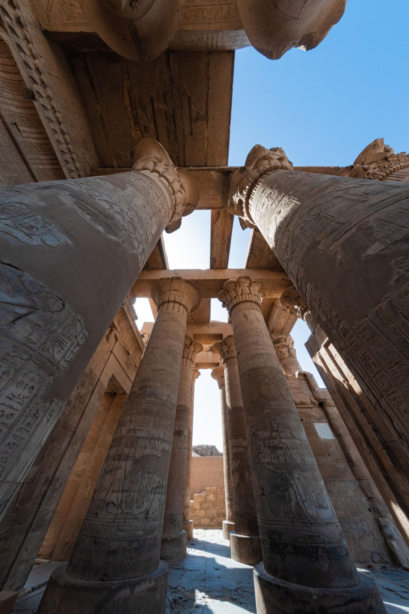 Upward view through carved columns to the preserved temple ceiling and blue sky.