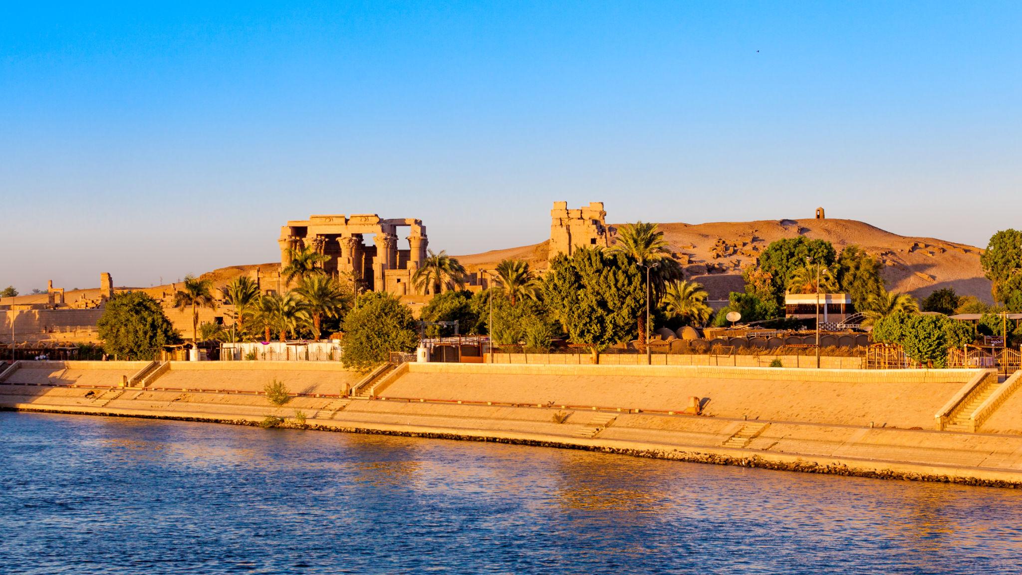 Kom Ombo Temple perched above the Nile riverbank, viewed from the river at sunset.