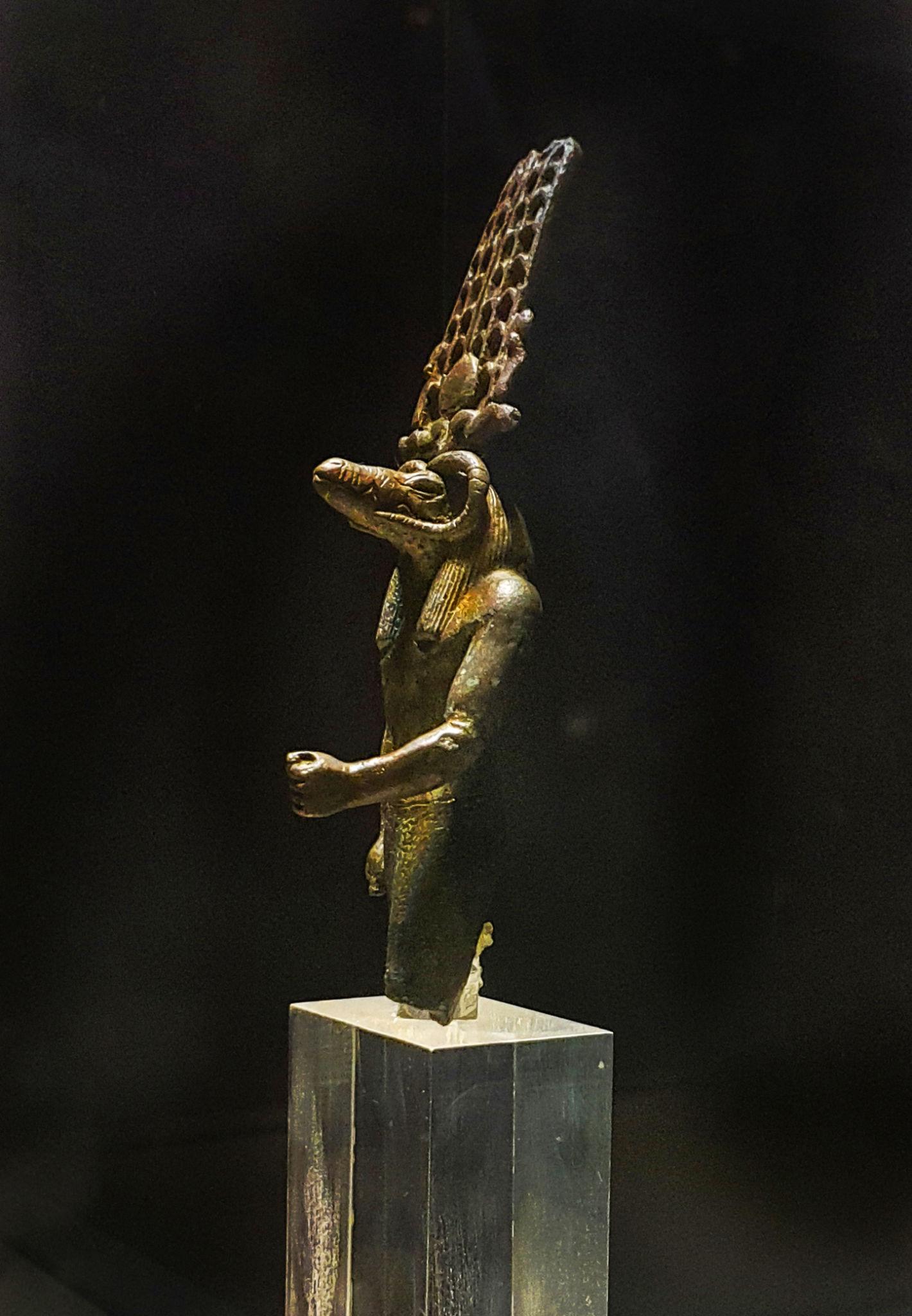 Bronze statuette of crocodile-headed god Sobek with tall plumed crown on display.
