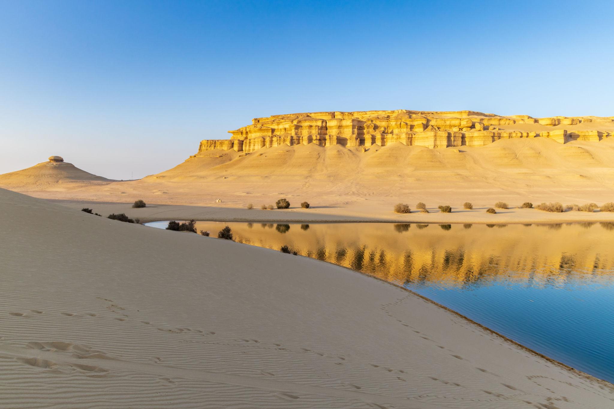 Golden sandstone cliffs and dunes reflected in a calm Lake Qarun inlet at sunrise, Fayoum