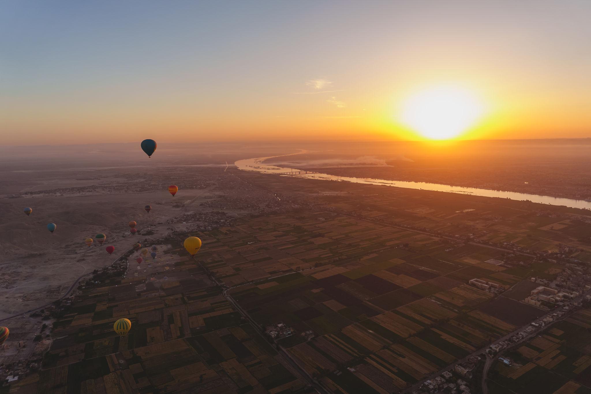 Aerial sunrise view of the Nile cutting through Luxor fields with balloons drifting above