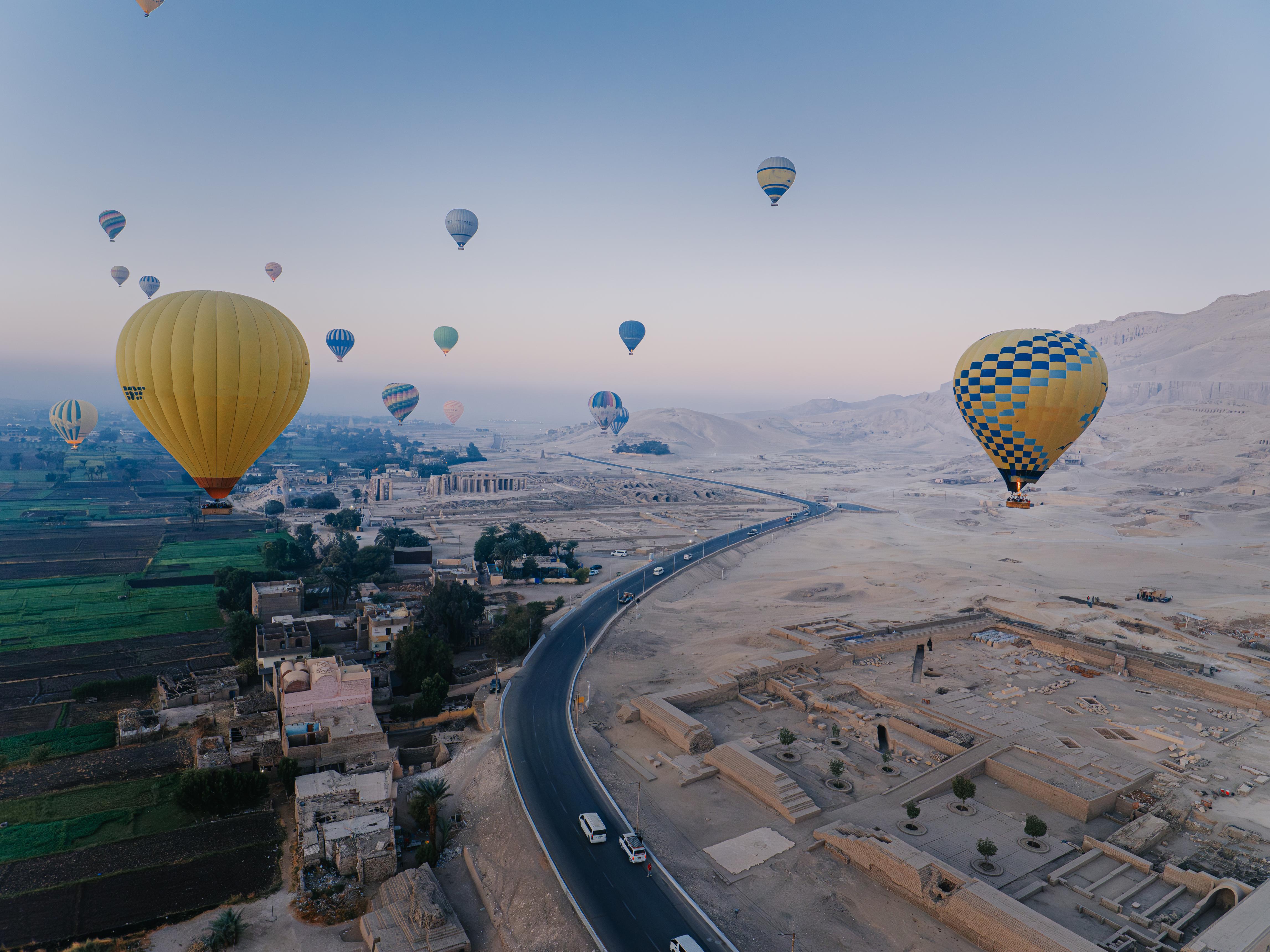 Yellow balloons hovering over the road between green fields and desert on Luxor's West Bank