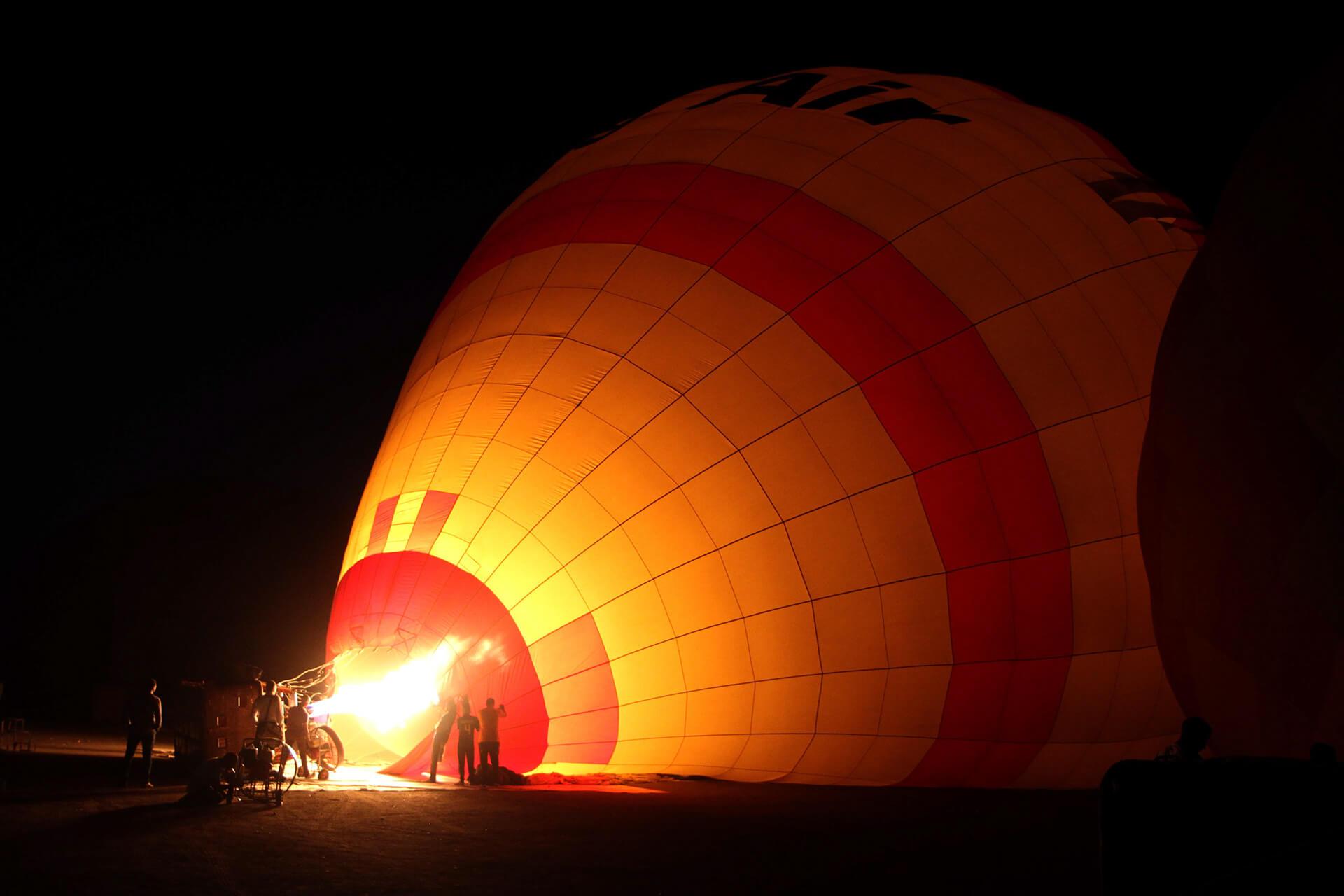 Burner firing a bright flame into a balloon during night inflation with crew silhouettes