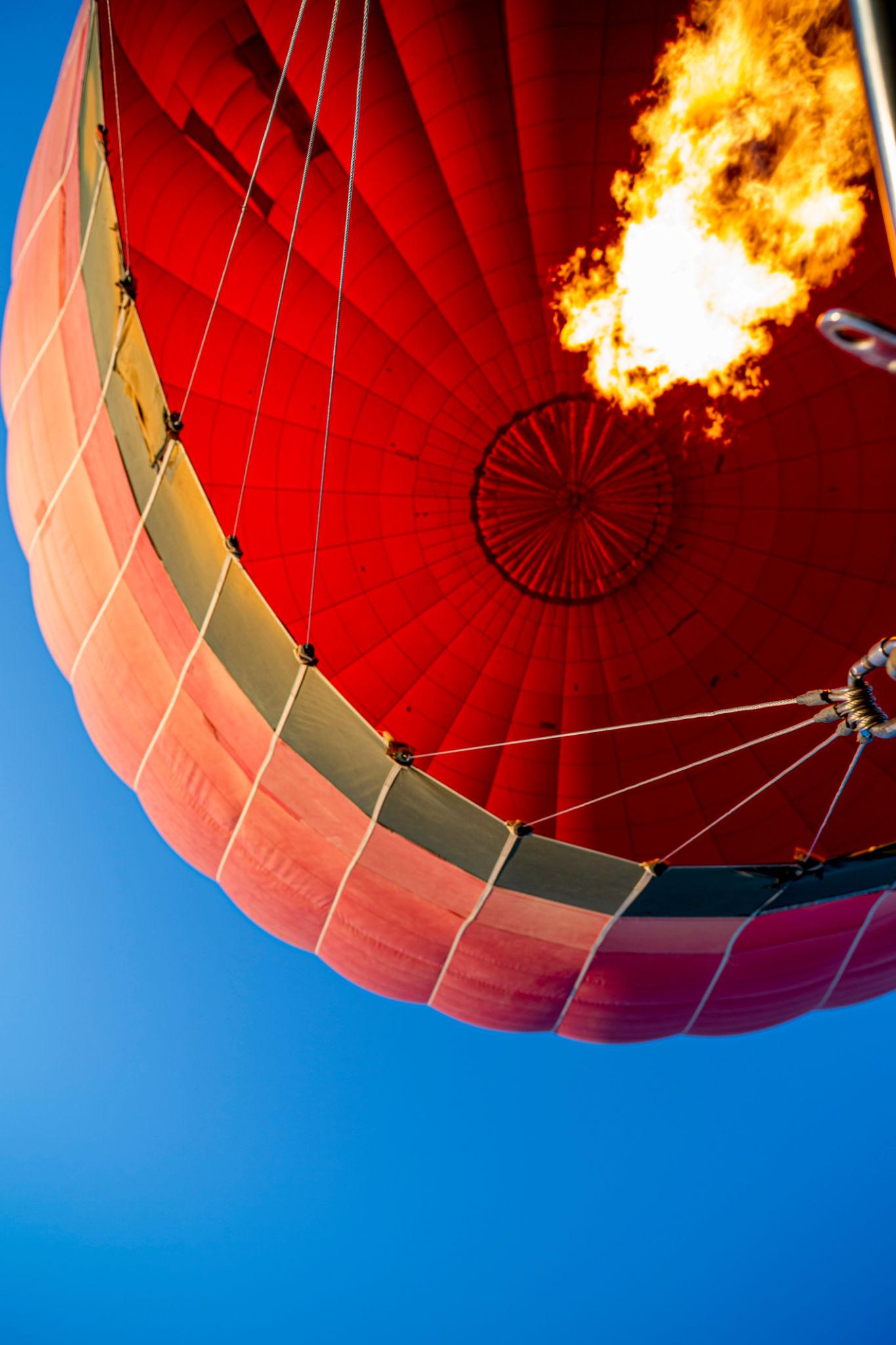 Close-up of a balloon's burner flame firing against the red canopy and clear blue sky