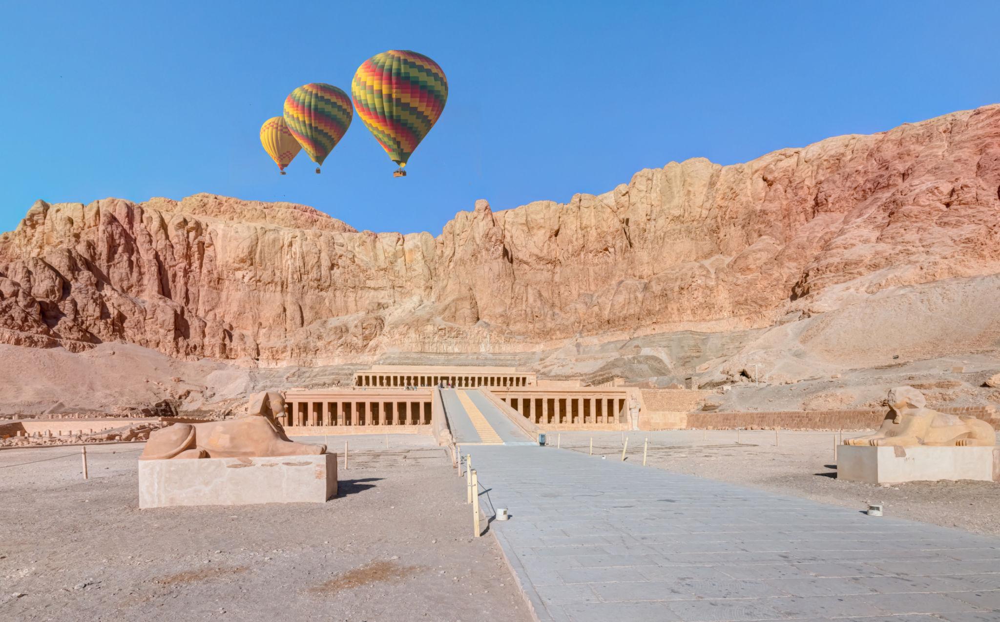 Two colorful balloons hovering above Hatshepsut Temple's cliffs on Luxor's West Bank