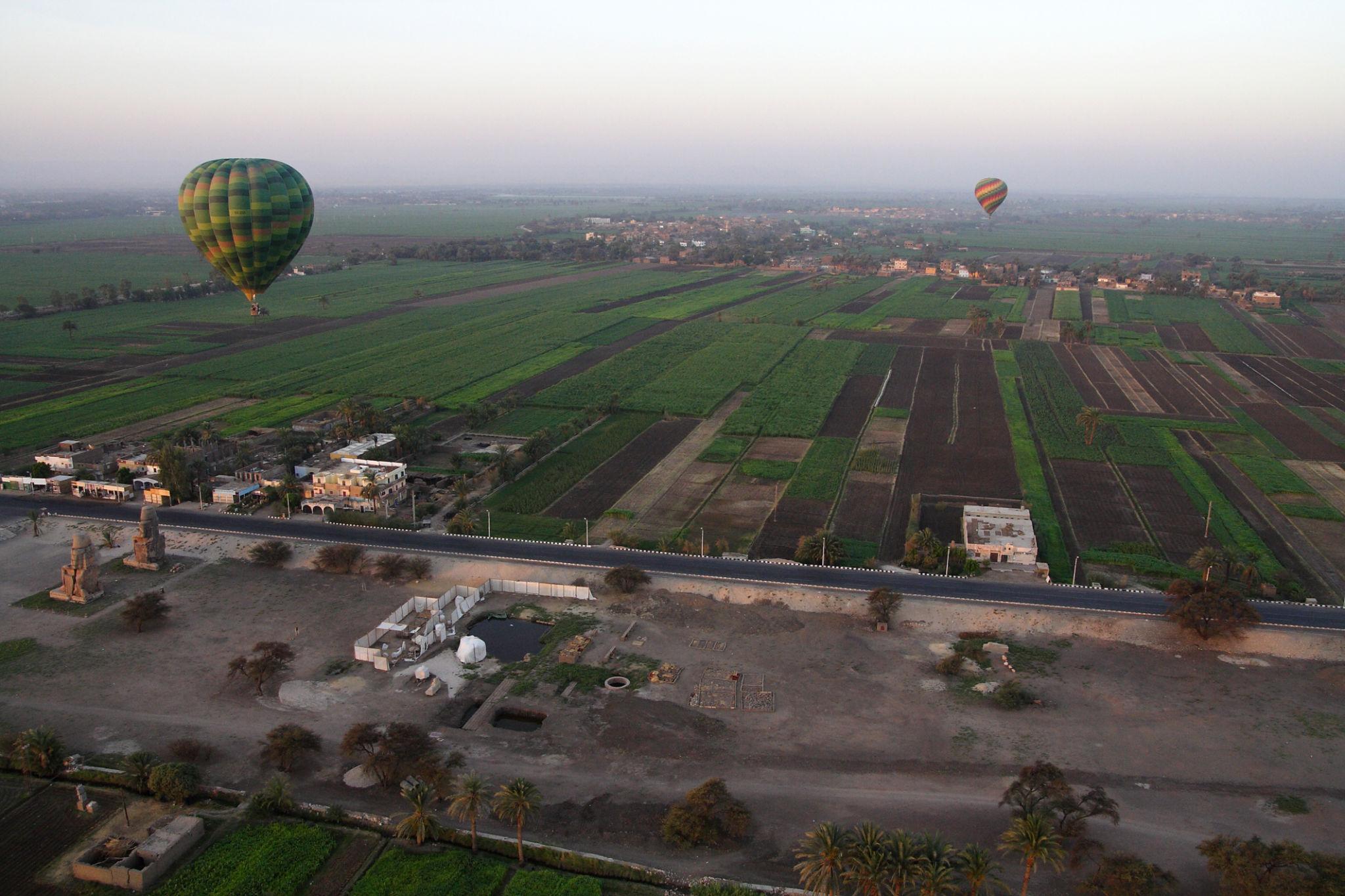 Hot air balloons gliding over patchwork fields near the Colossi of Memnon in Luxor