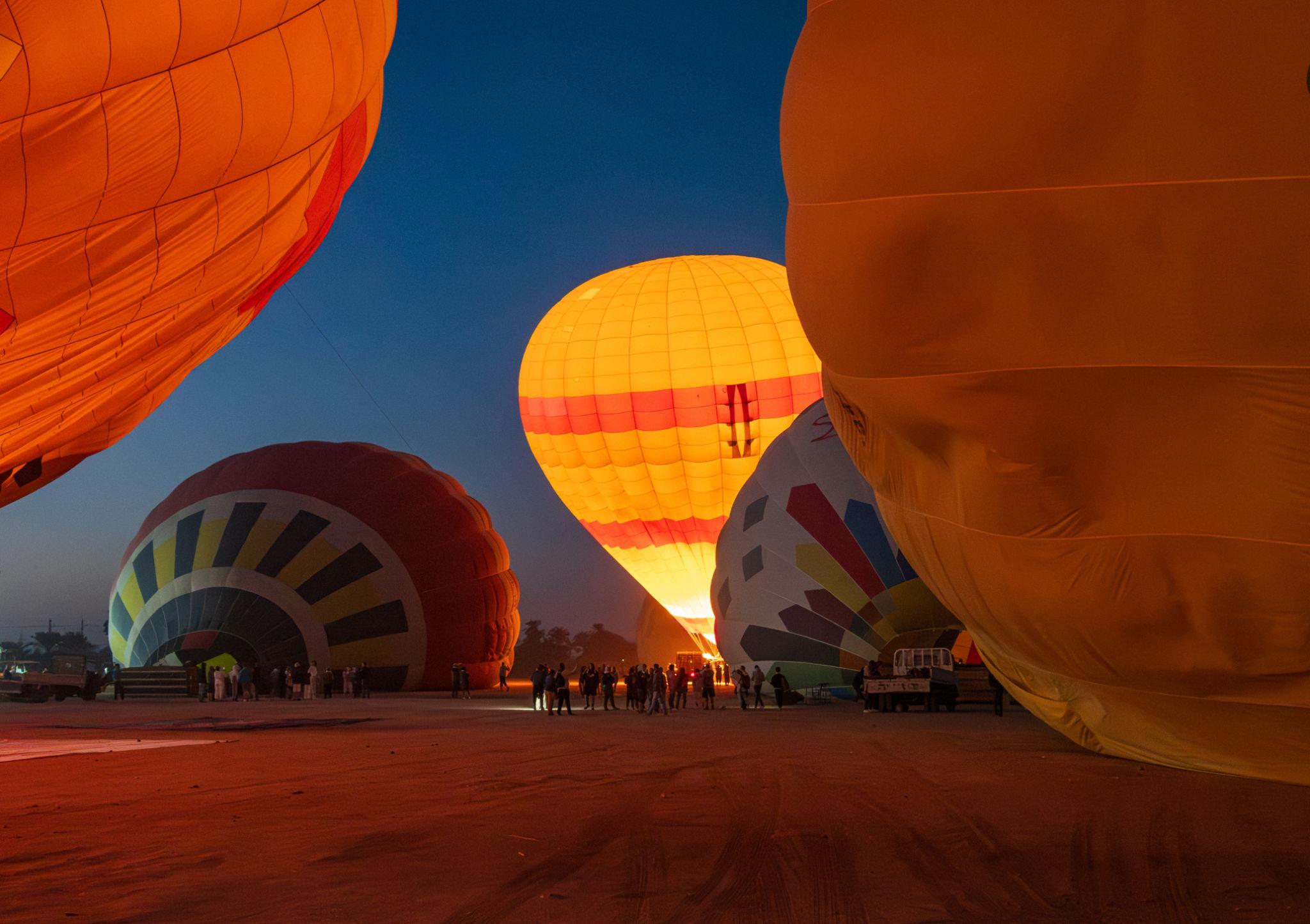 Balloons illuminated by burner flames during pre-dawn inflation at the Luxor launch field