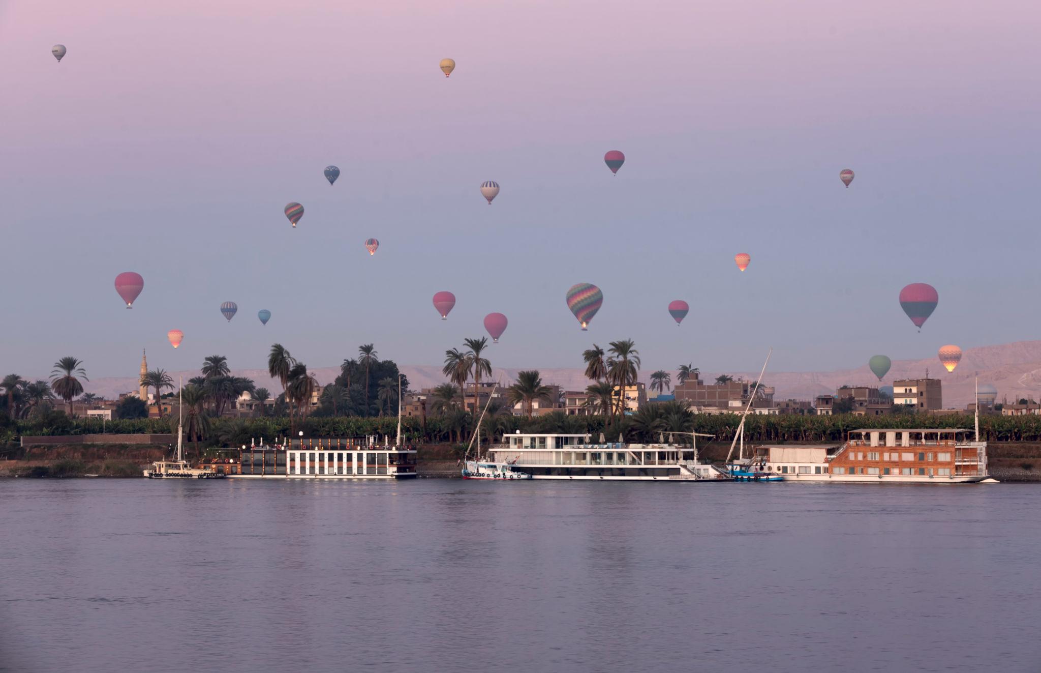 Dozens of hot air balloons over the Nile with moored cruise ships at dawn in Luxor