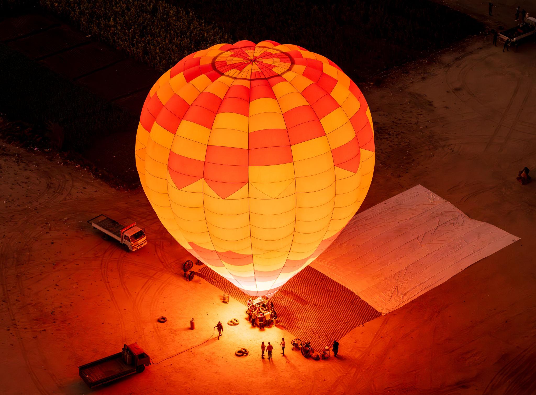 Orange balloon fully inflated and glowing at the pre-dawn Luxor launch site