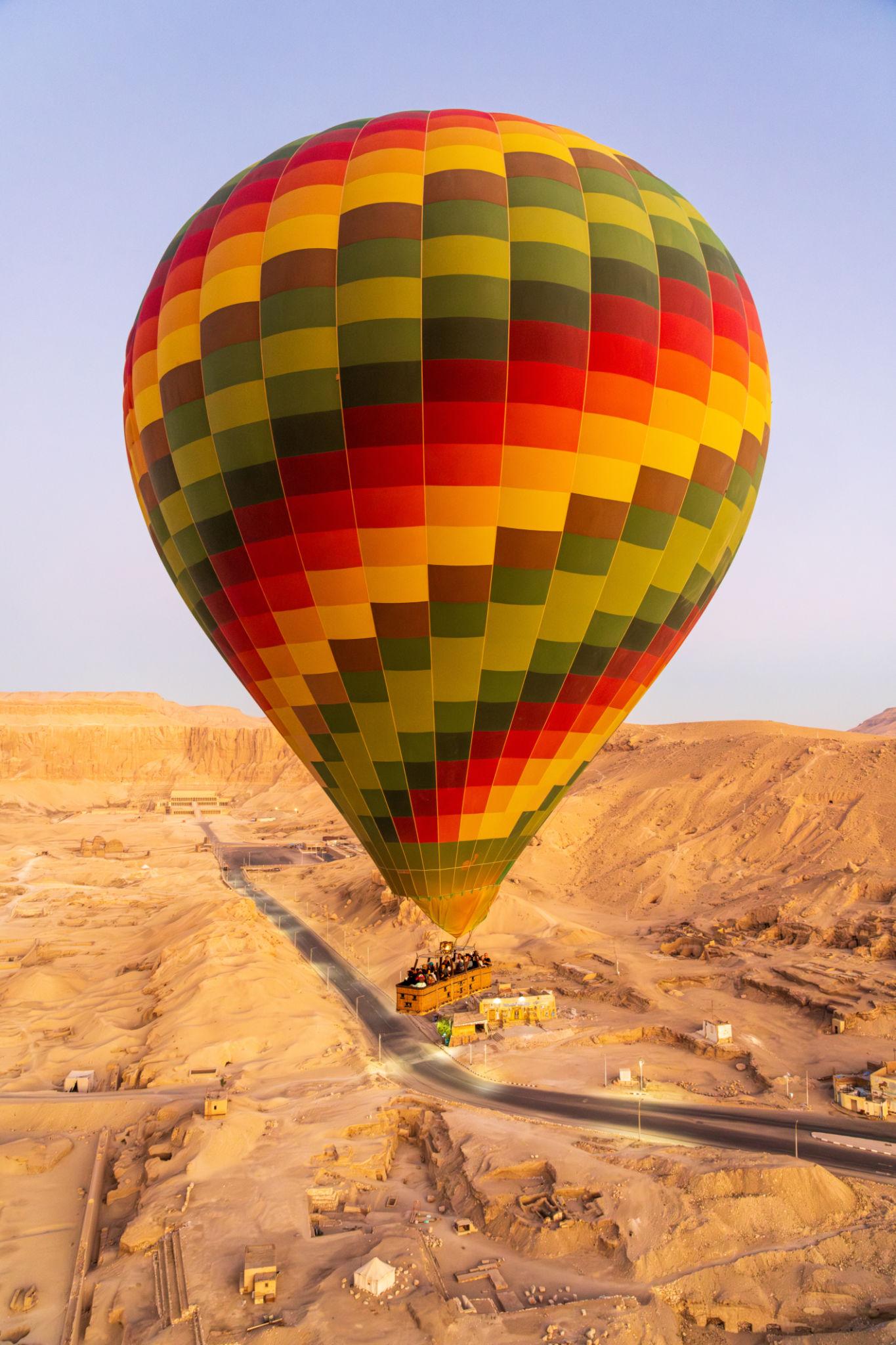 Colorful rainbow-patterned hot air balloon floating low over Luxor's desert West Bank