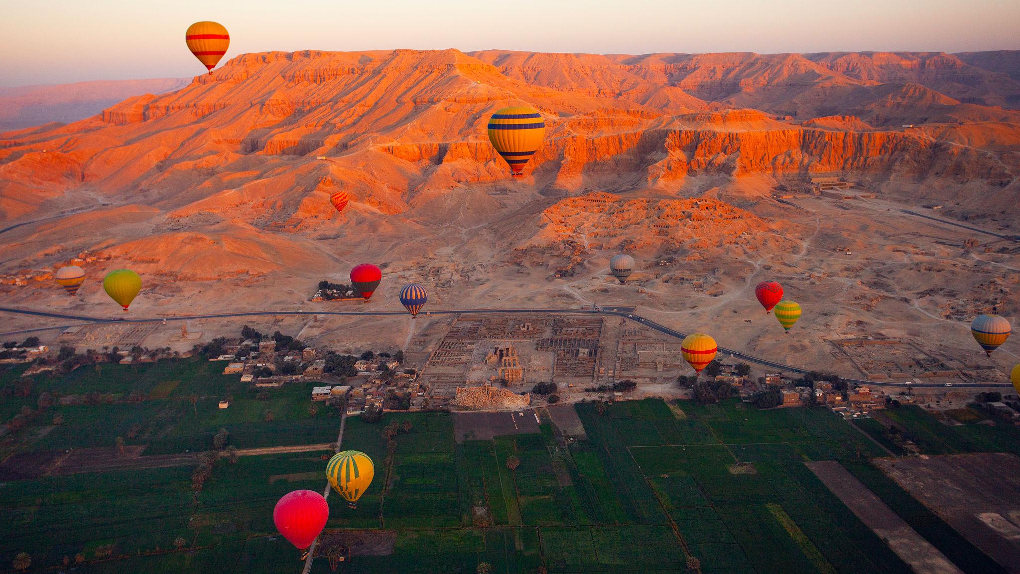 Many balloons floating above Ramesseum temple ruins with red Theban mountains behind
