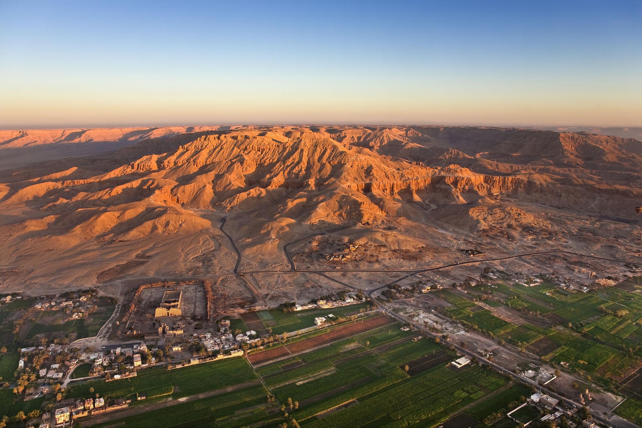 Aerial view of the Theban mountains glowing in sunrise light above Luxor's green valley