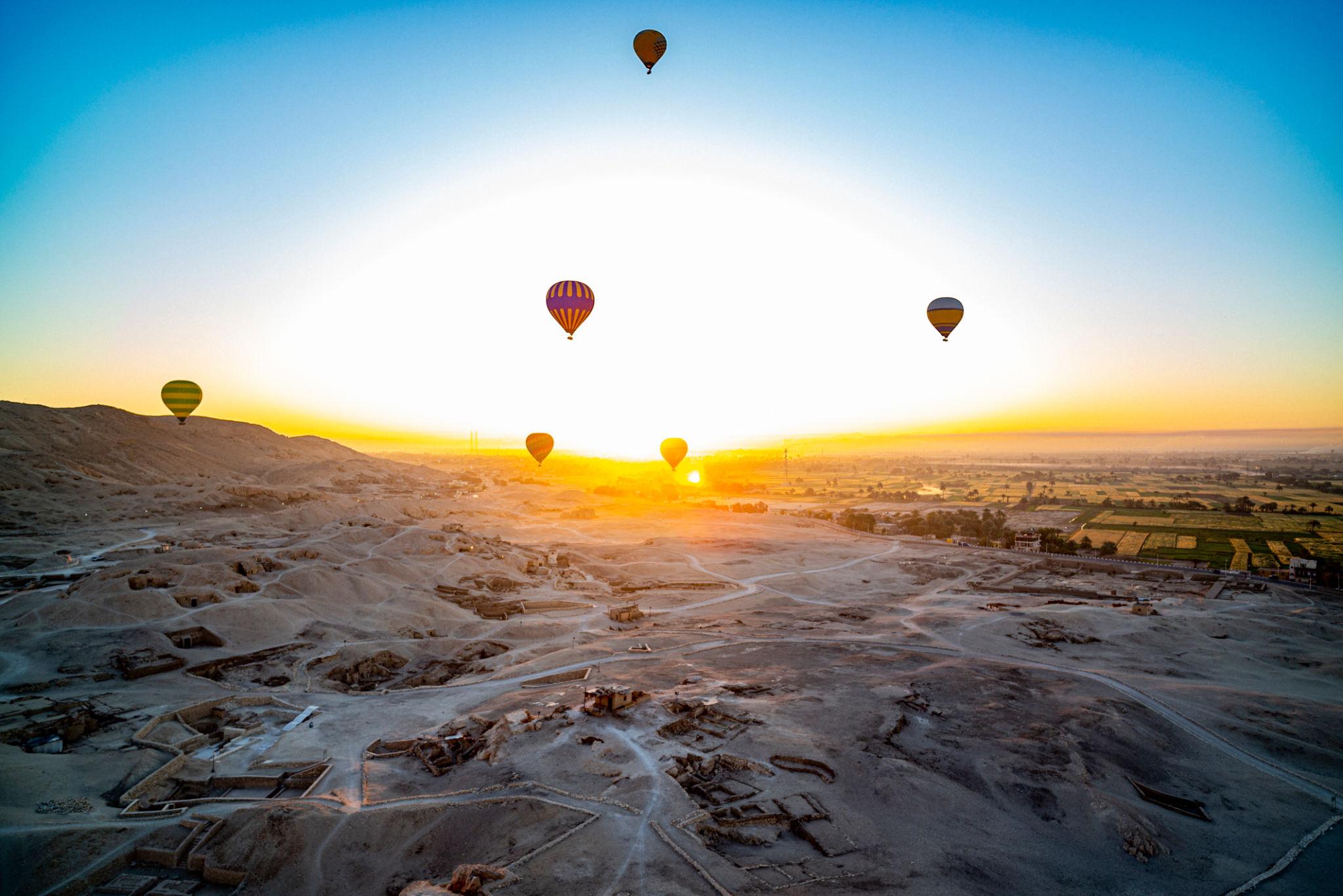 Balloons scattered across a vivid sunrise above the Valley of the Kings tomb hills
