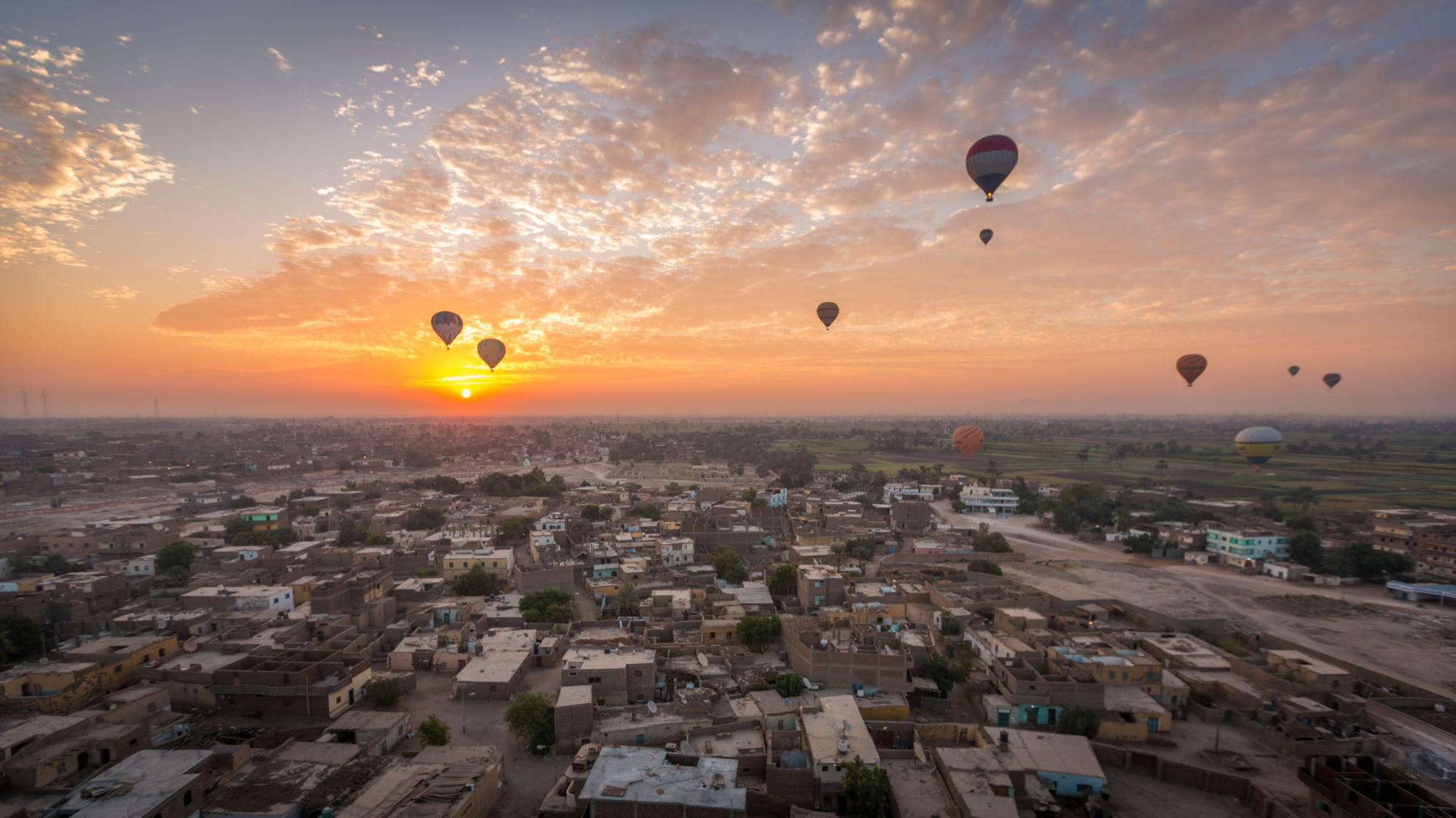 Balloons scattered over a Luxor West Bank village at sunrise with a streaked orange sky