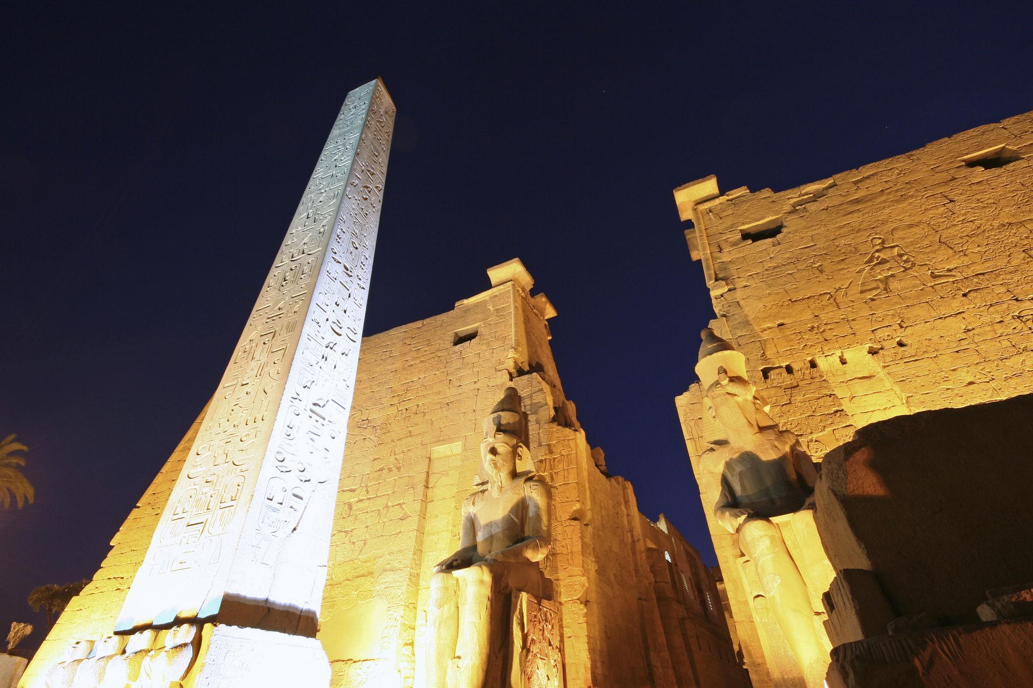 Low-angle night view of the Luxor obelisk and pylon with hieroglyphs.