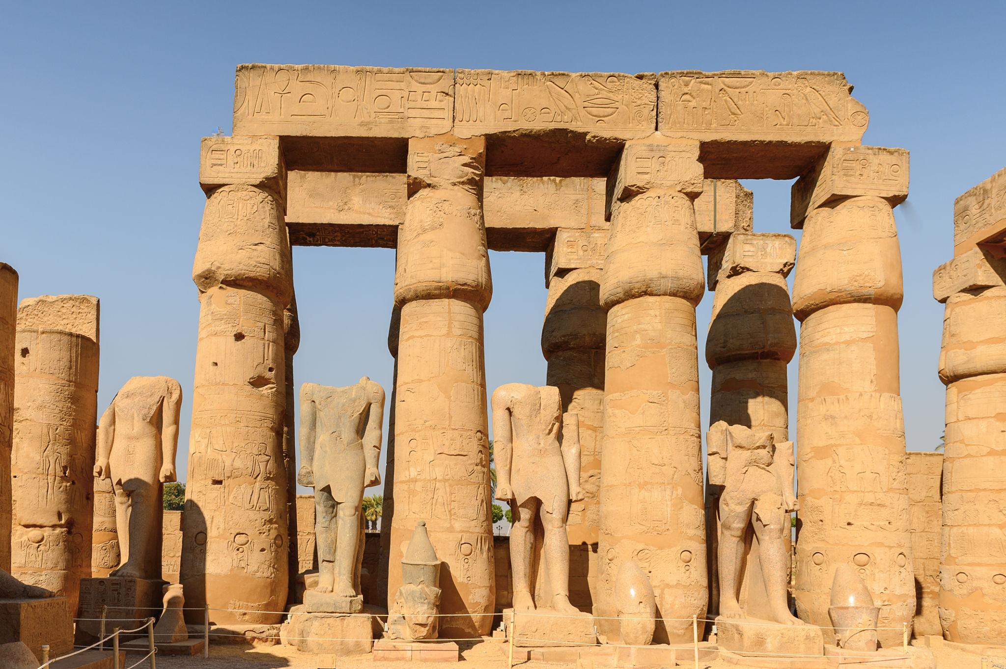 Osirid statues and columns inside Luxor Temple courtyard in daylight.