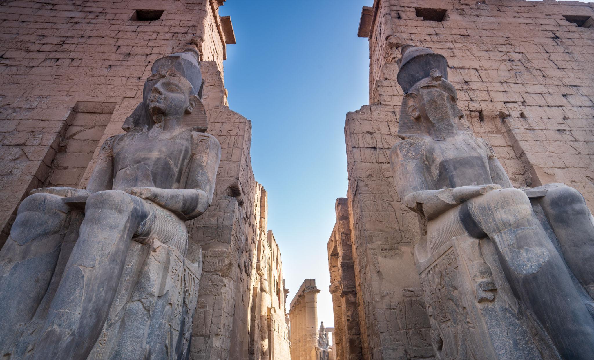 Two Ramses II colossi flanking the pylon gateway under blue sky.