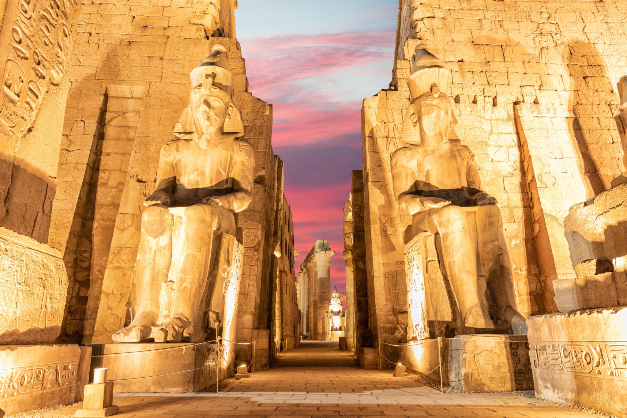 Ramses II colossi framing the pylon entrance against a pink sunset sky.