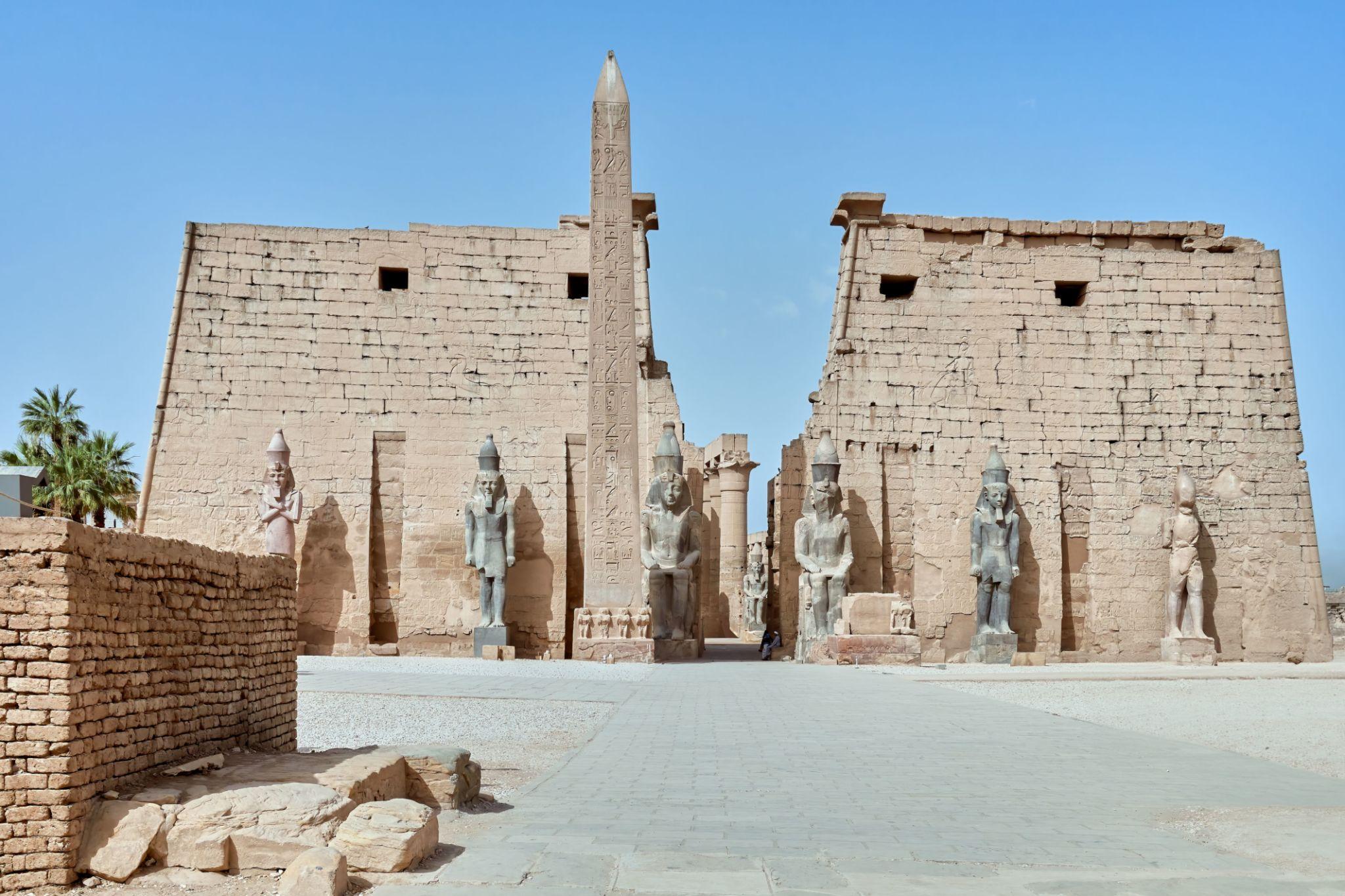Daylight view of Luxor Temple pylon facade with obelisk and statues.