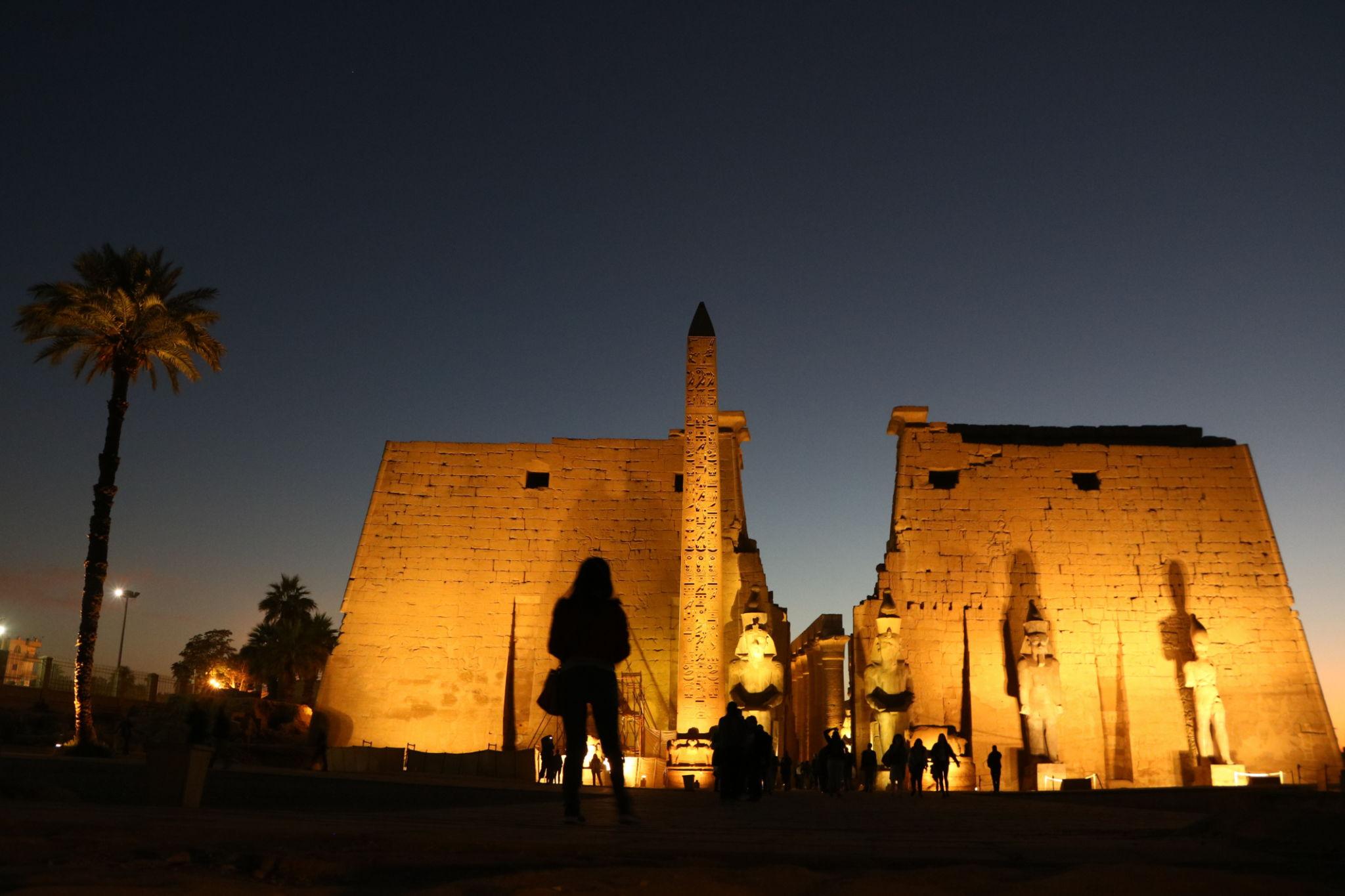 Luxor Temple pylon with obelisk and Ramses statues illuminated at twilight.
