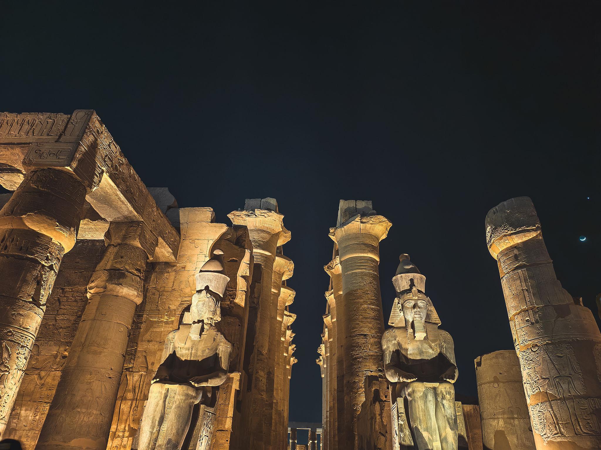 Colossal Ramses II statues amid columns in the courtyard by night.