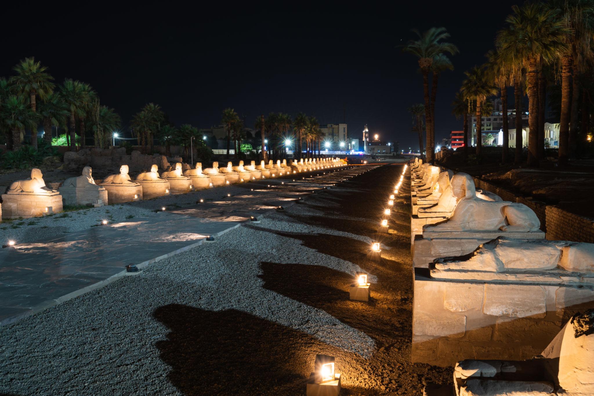 Restored Avenue of Sphinxes stretching toward Luxor city lights at night.