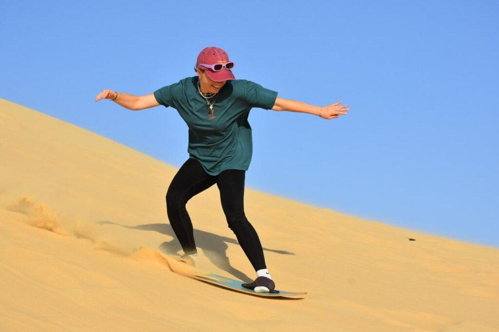 Traveler balancing on a sandboard carving down a golden desert dune