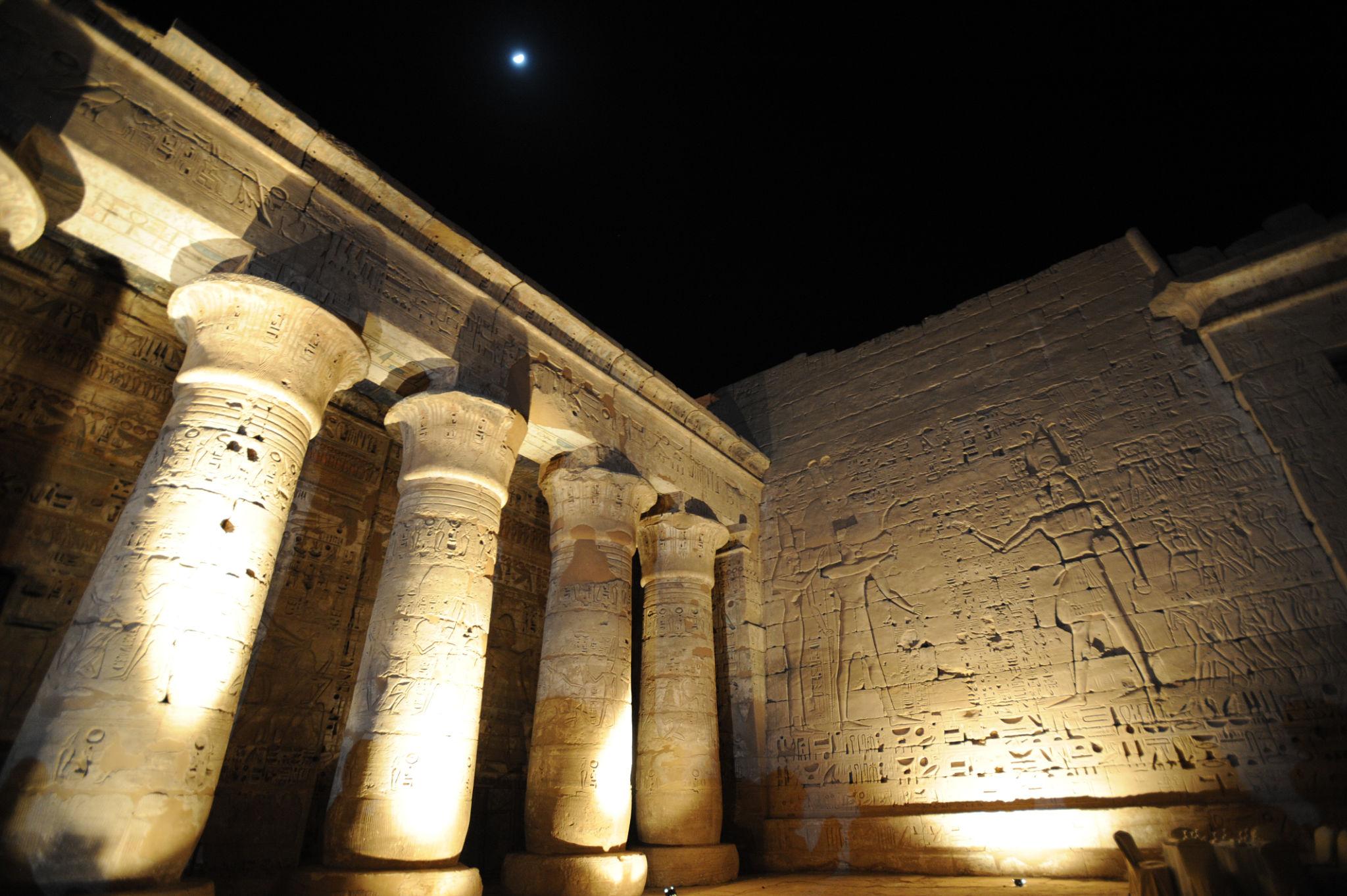 Illuminated hypostyle columns of Medinet Habu at night beneath a moonlit sky.