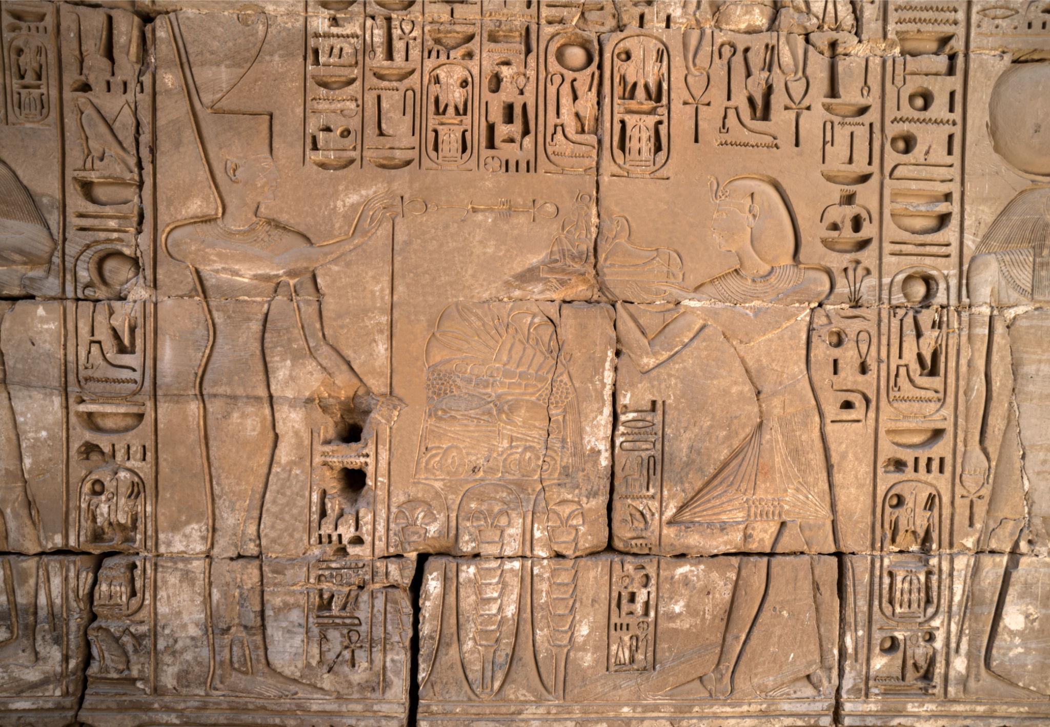 Close-up of detailed sunken hieroglyphs and figural reliefs on a Medinet Habu wall.