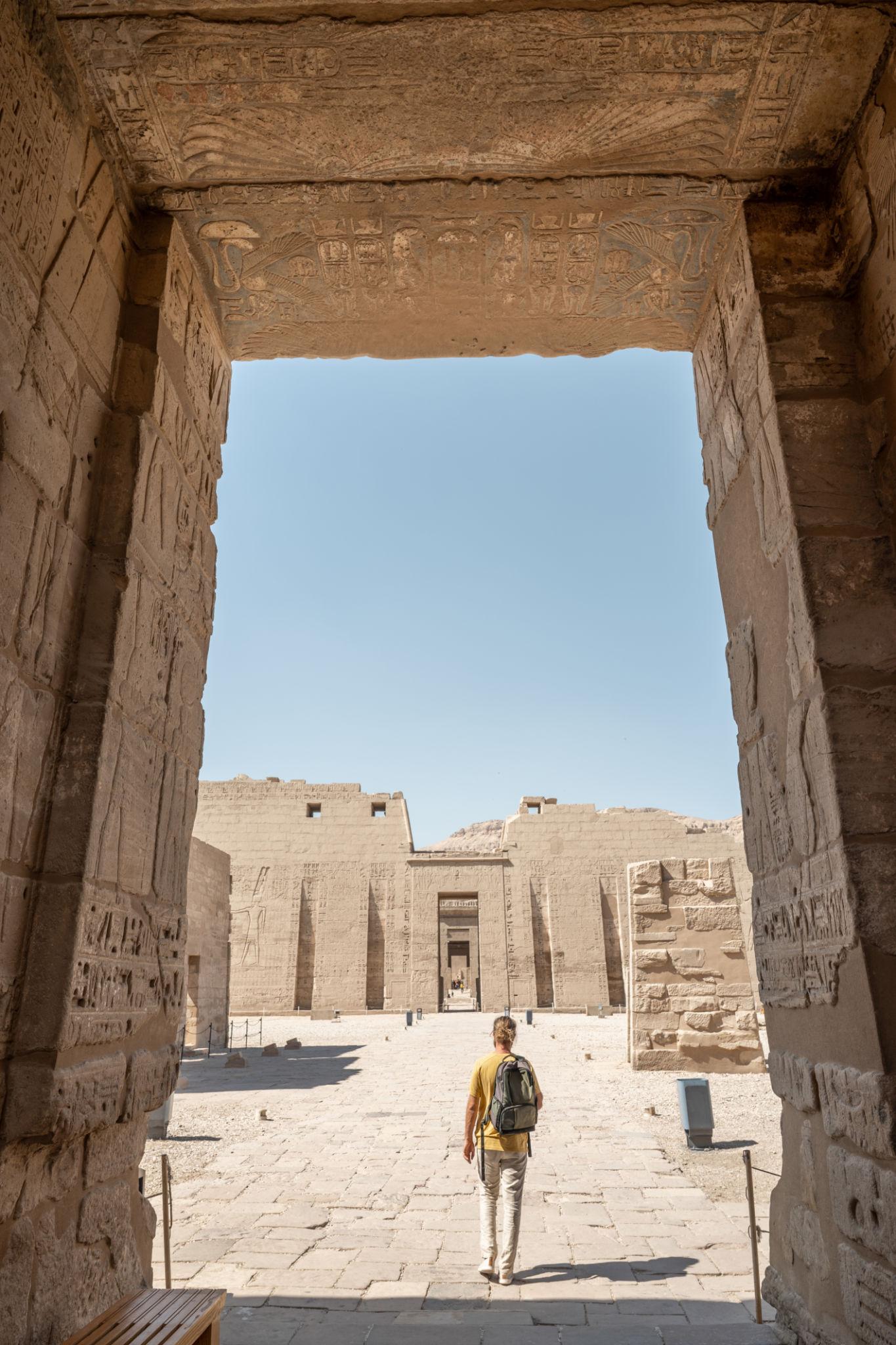 Visitor framed by the Migdol gateway looking toward the first pylon of Medinet Habu.