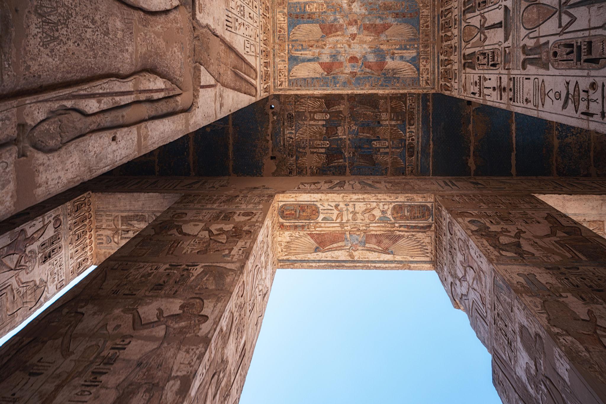 Dramatic upward view of painted temple ceiling and open sky at Medinet Habu.