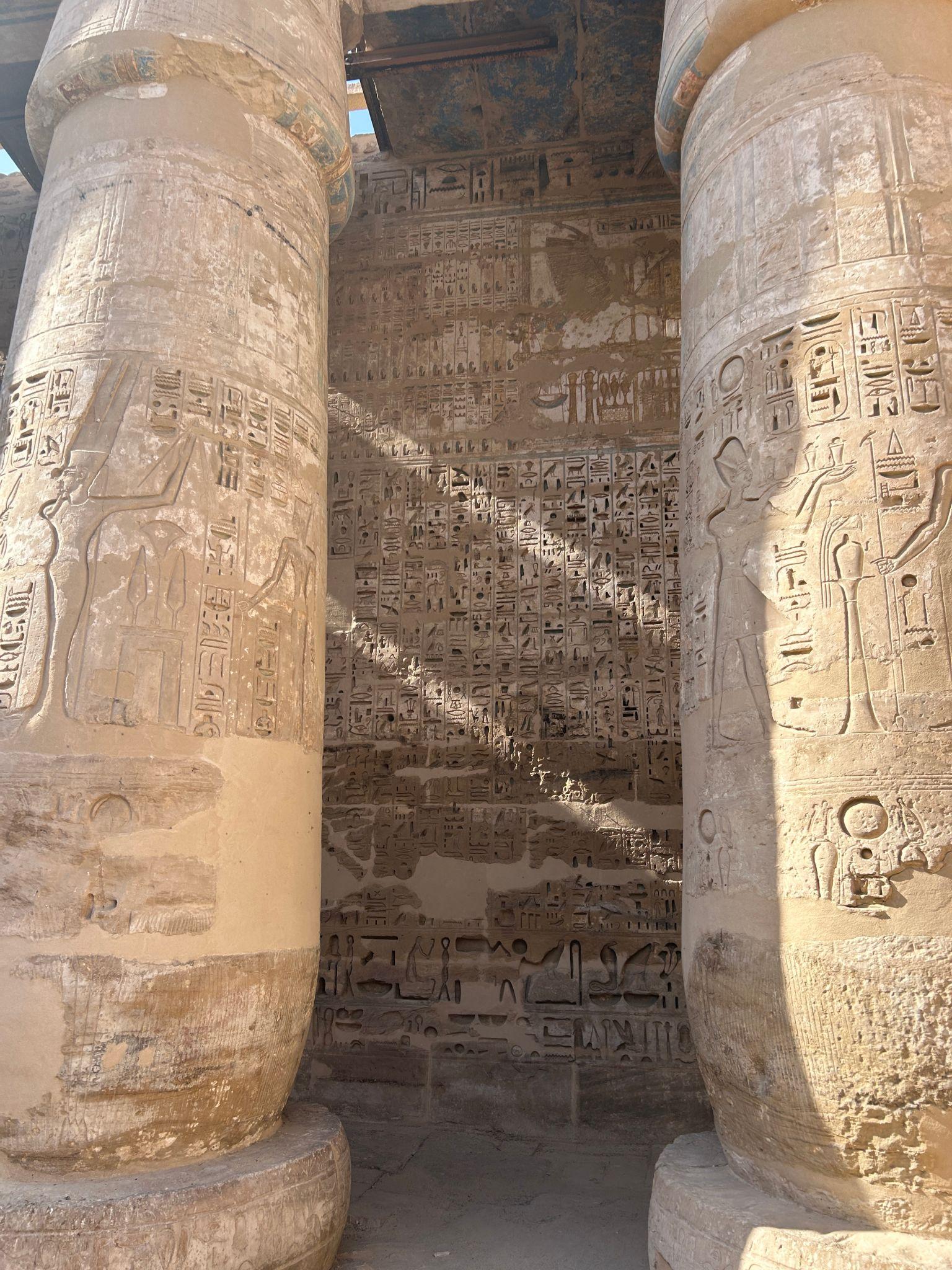 Sunlight streaming between hieroglyph-covered columns inside Medinet Habu temple.