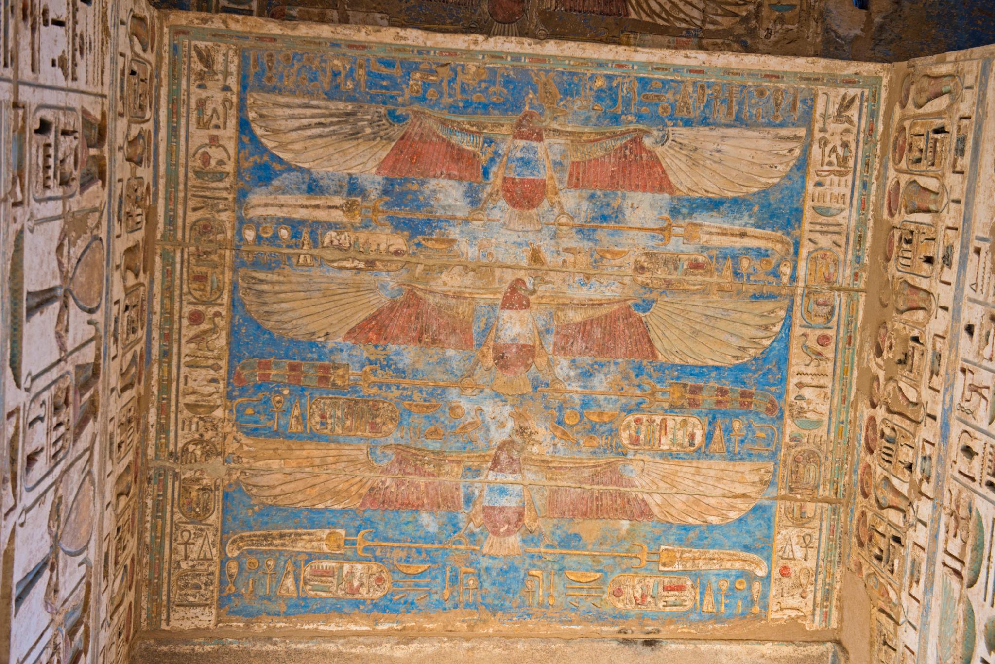 Vivid ceiling fresco of winged Nekhbet goddesses in red, blue and ochre at Medinet Habu.