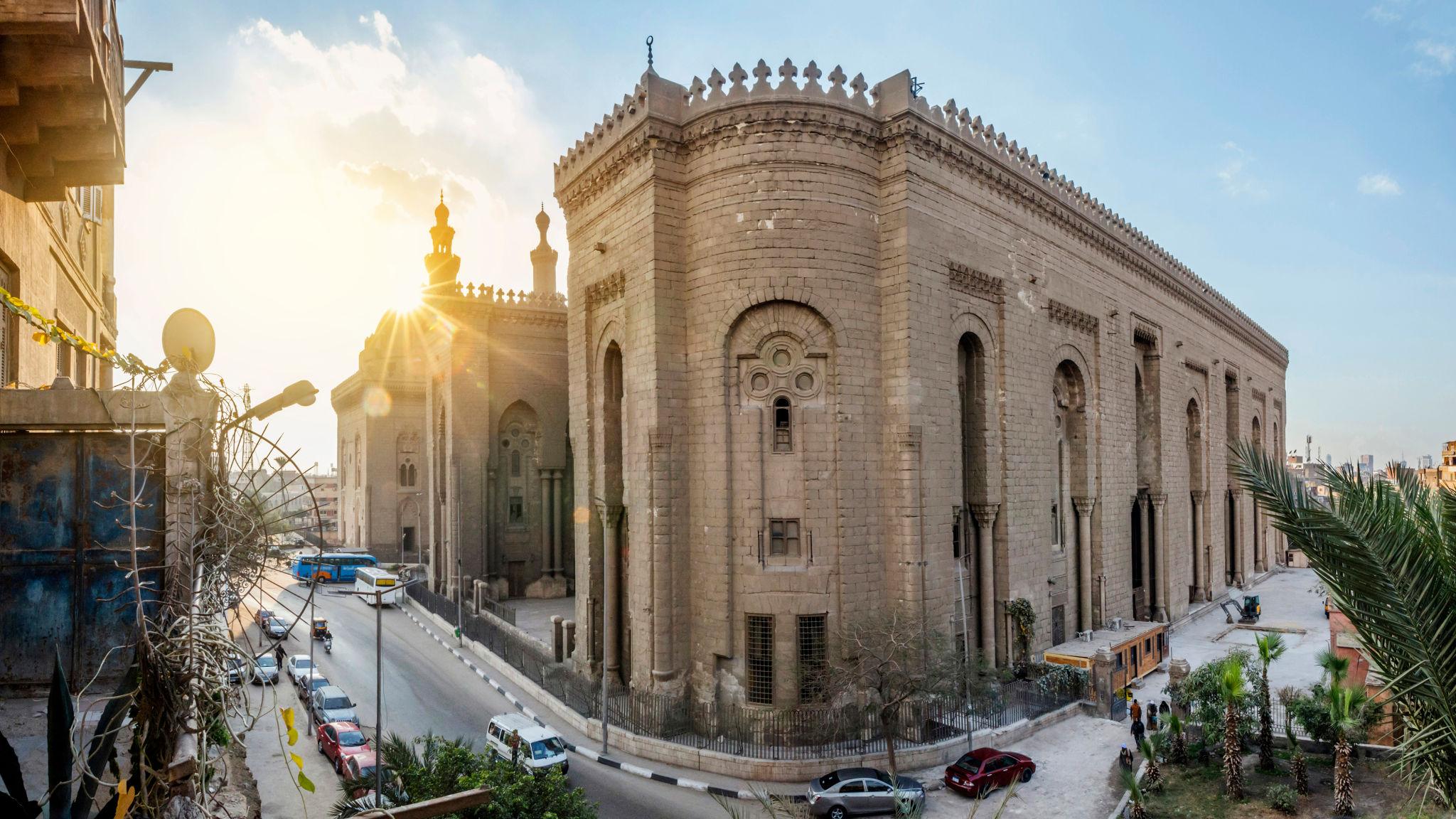 Massive stone exterior facade and minarets of the Sultan Hassan mosque at sunset