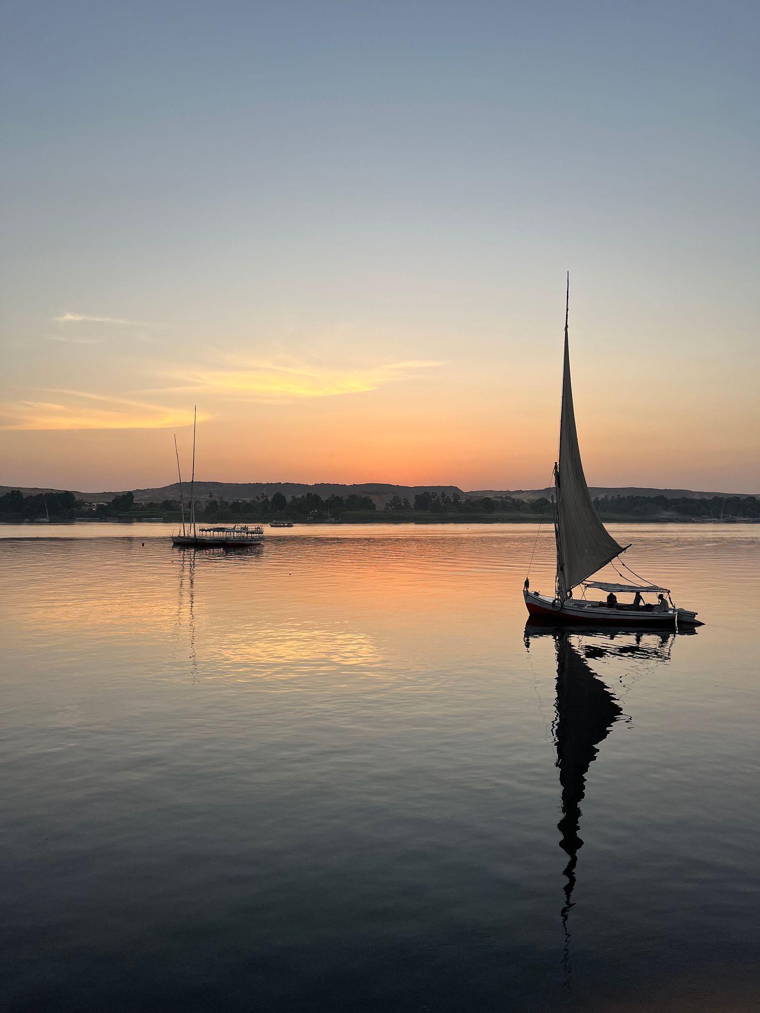 Feluccas reflected in glassy Nile waters at sunset near Aswan.