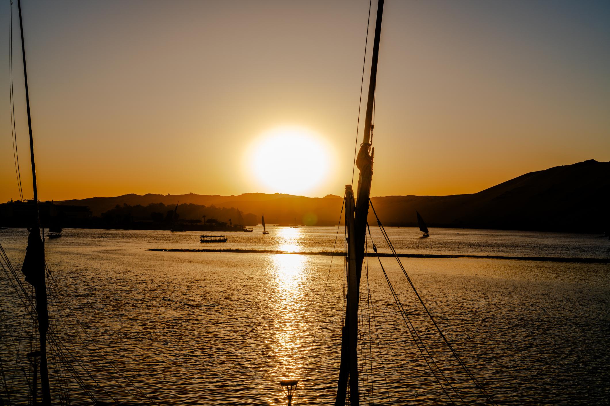 Sun setting over the Nile framed by felucca masts and rigging in Aswan.