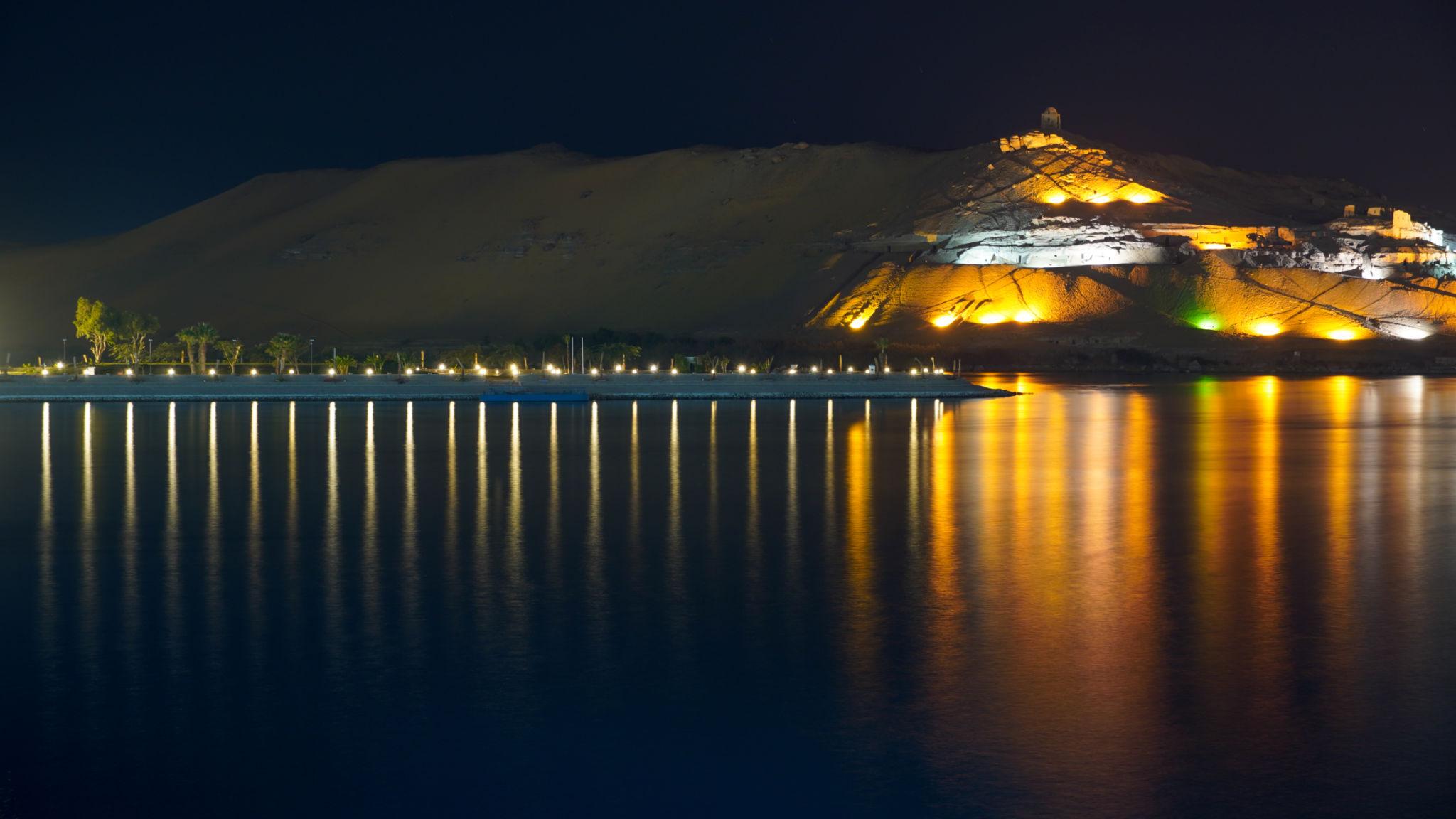 Illuminated sand dune and desert bank reflected in the Nile at night in Aswan.