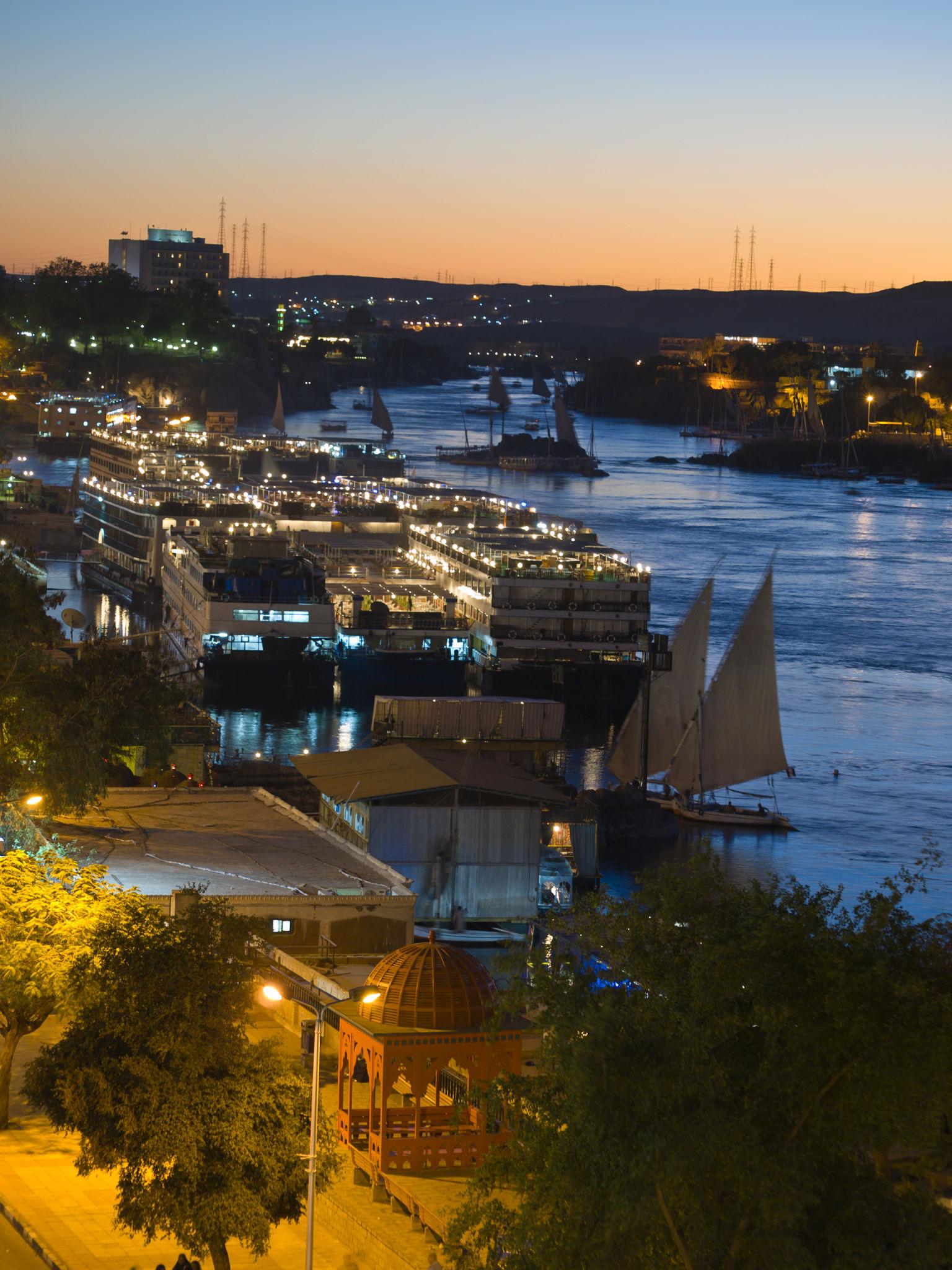 Fleet of cruise boats and a felucca moored along the Aswan waterfront at twilight.