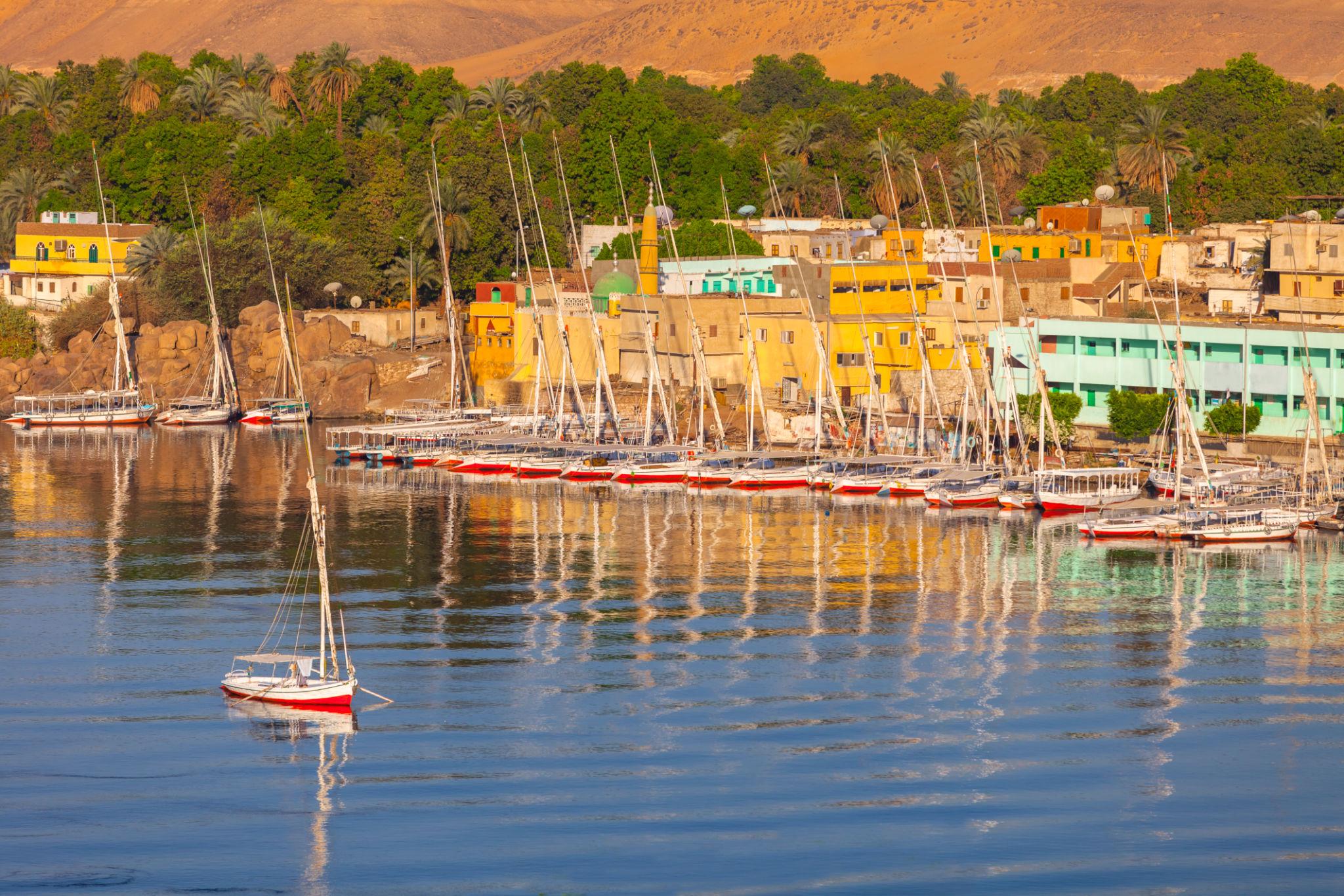 Colorful Nubian-style houses lining the Nile bank with feluccas moored in Aswan.