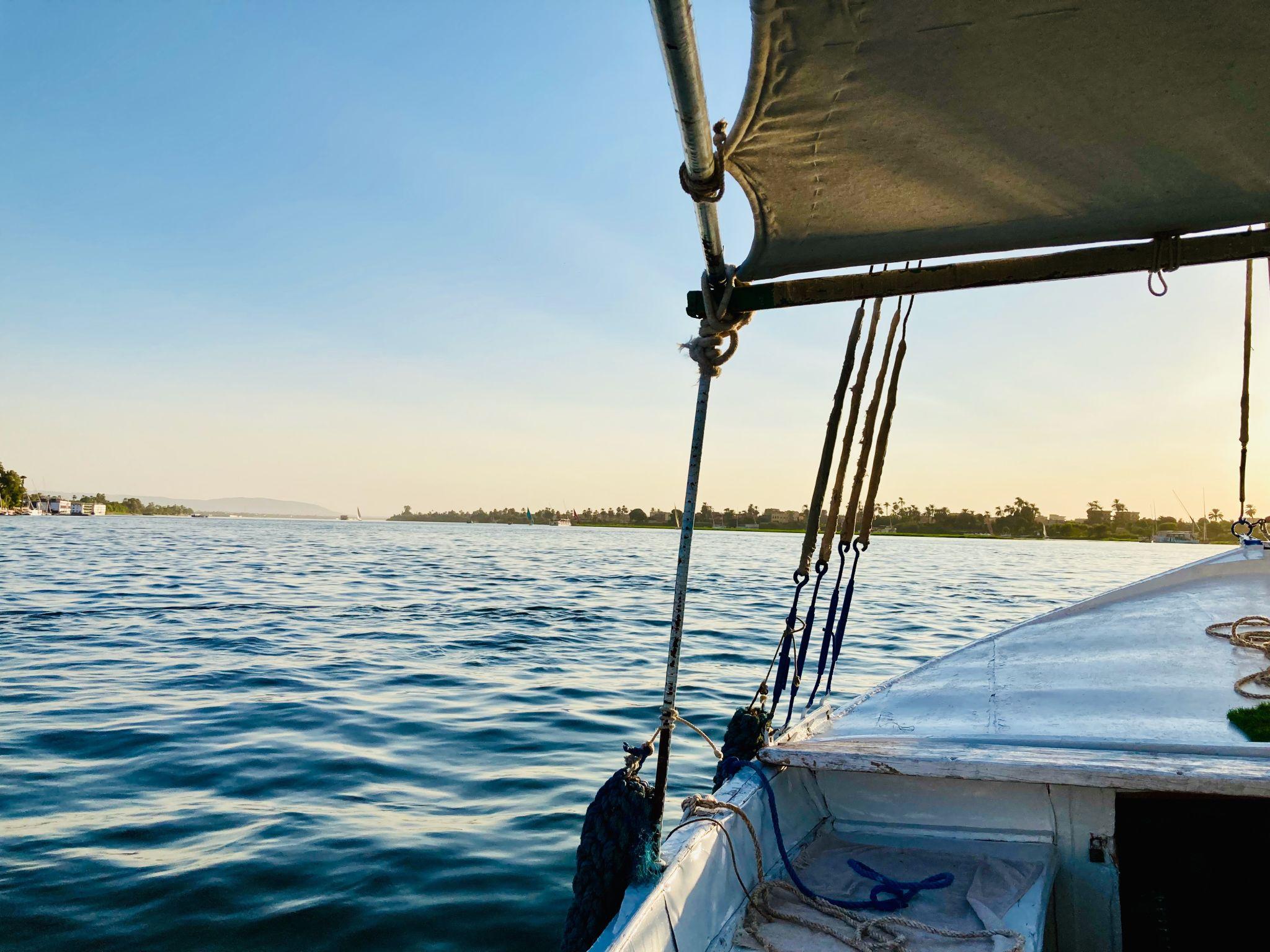 Onboard felucca view across calm Nile waters toward the Luxor shoreline