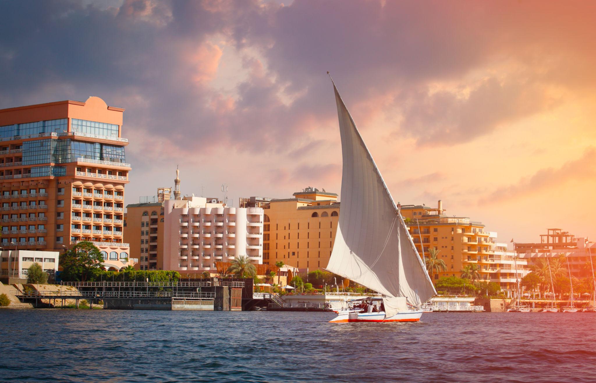 Felucca sailing past Luxor hotel skyline under pastel sunset sky