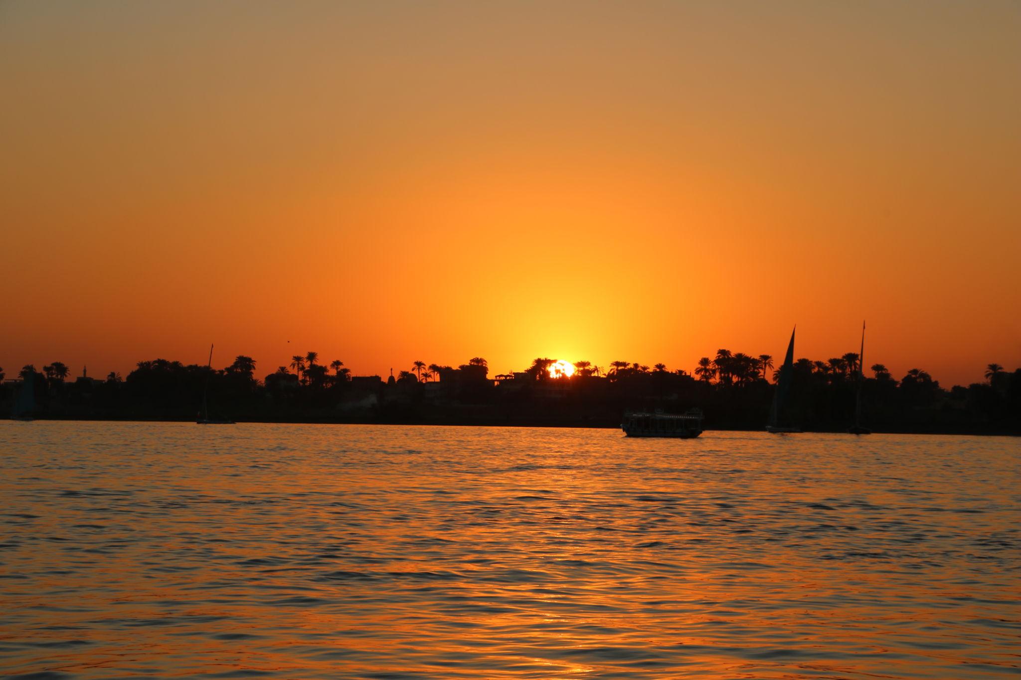 Glowing orange sunset over the Nile with boat and palm silhouettes