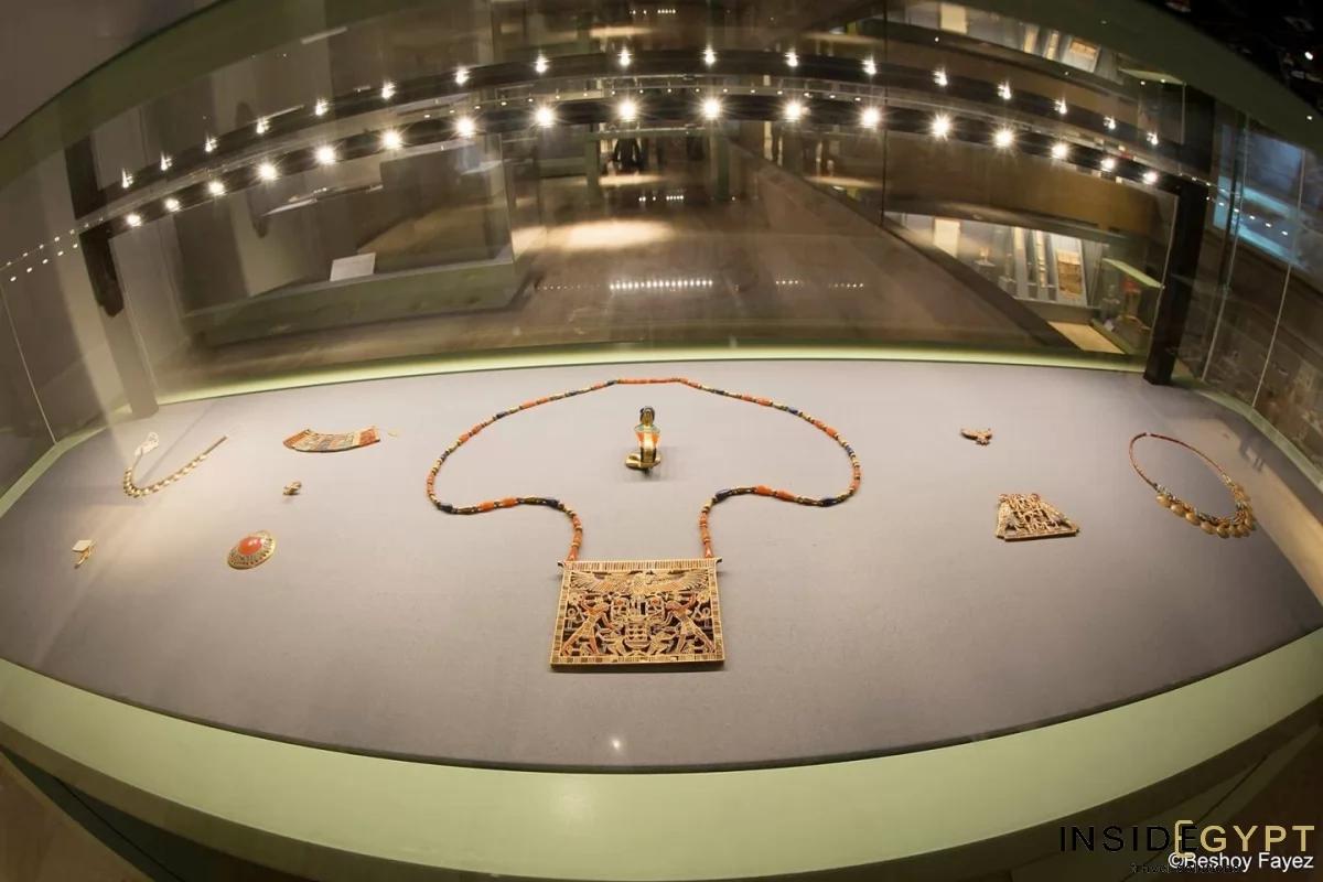 Ancient Egyptian jewelry and pectoral pieces laid out in a curved glass display case at NMEC