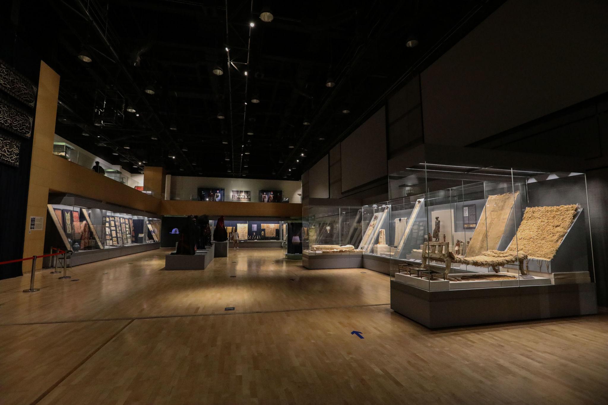 Spacious NMEC gallery with lit display cases showing ancient Egyptian textiles and artifacts