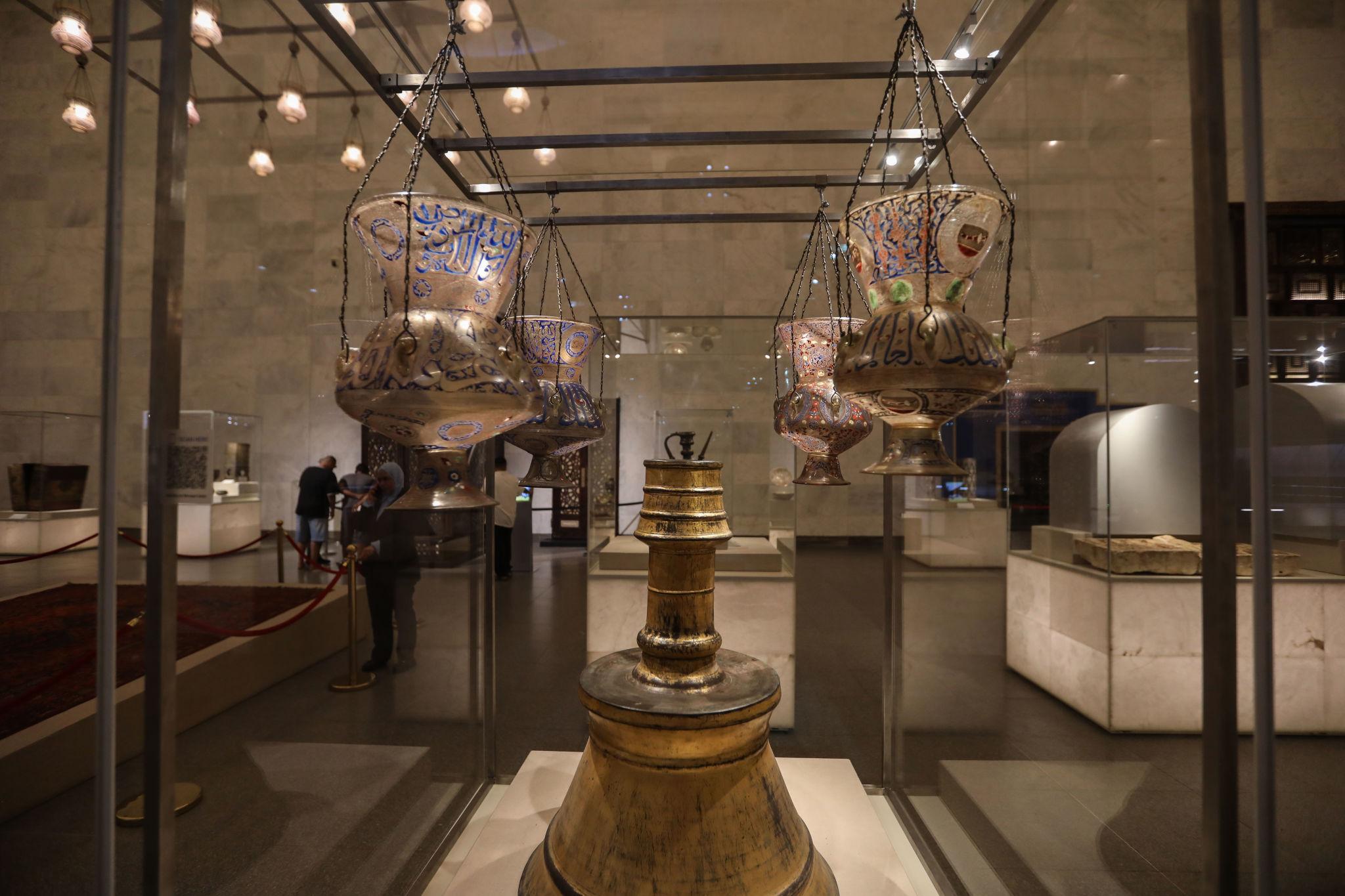 Ornate gilded and enameled Mamluk glass mosque lamps with Arabic calligraphy hang in a museum case